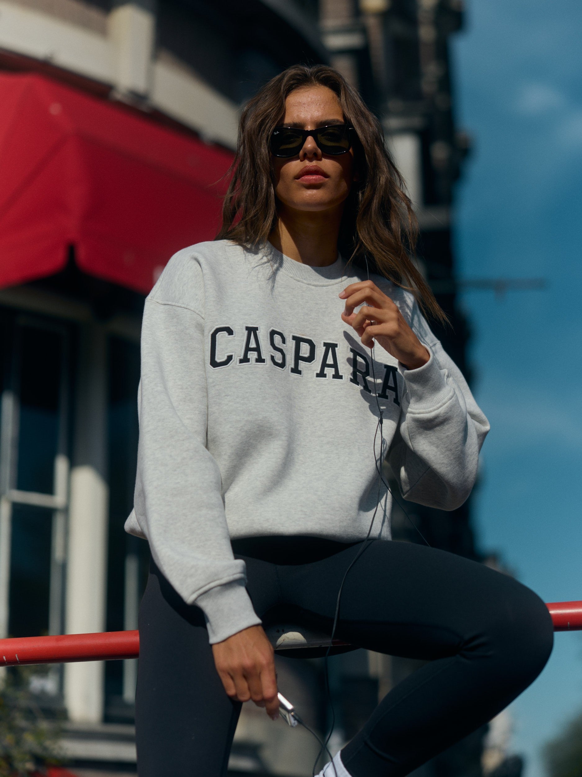 Woman wearing a grey melange CASPARA graphic crewneck sweatshirt and sunglasses outdoors.