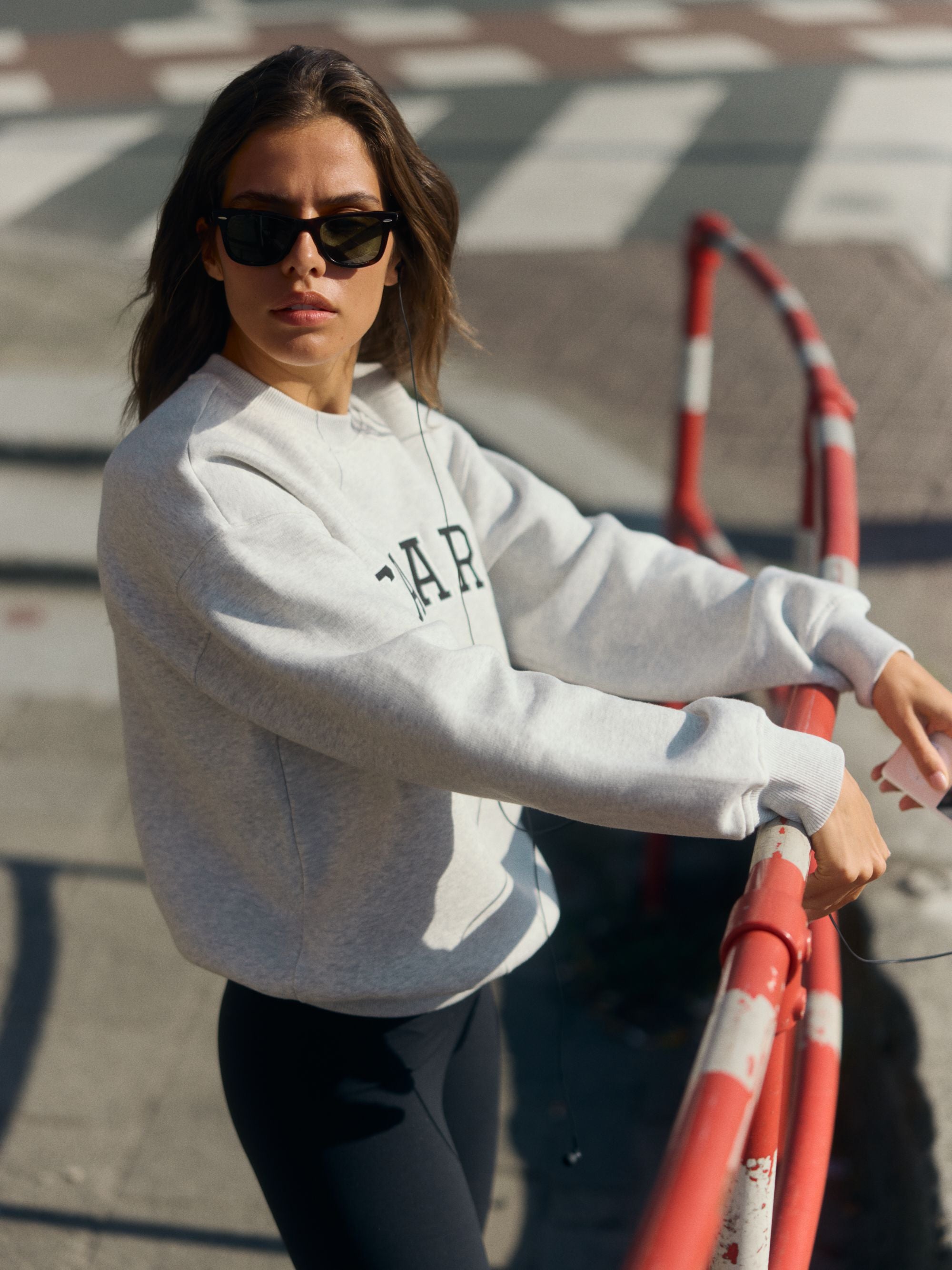 Woman wearing a grey melange oversized crewneck sweatshirt and sunglasses on a city street.