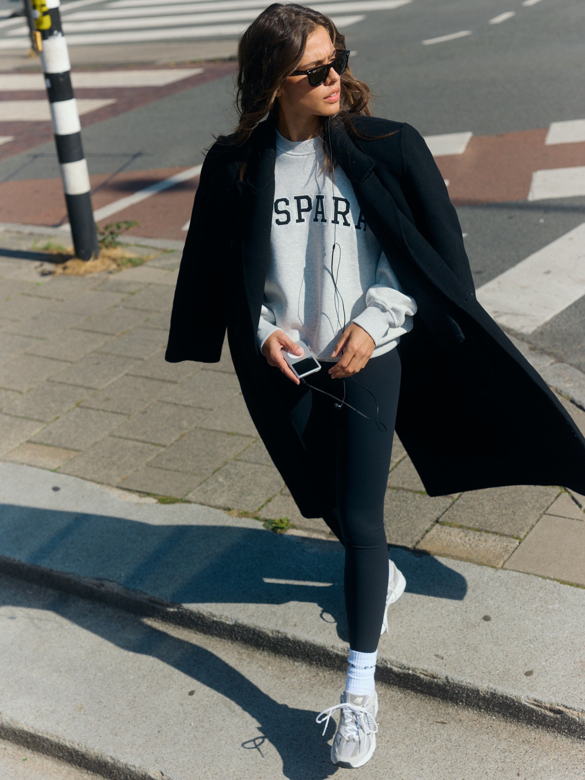Woman wearing a grey melange crewneck sweatshirt and black coat walking on a city street.