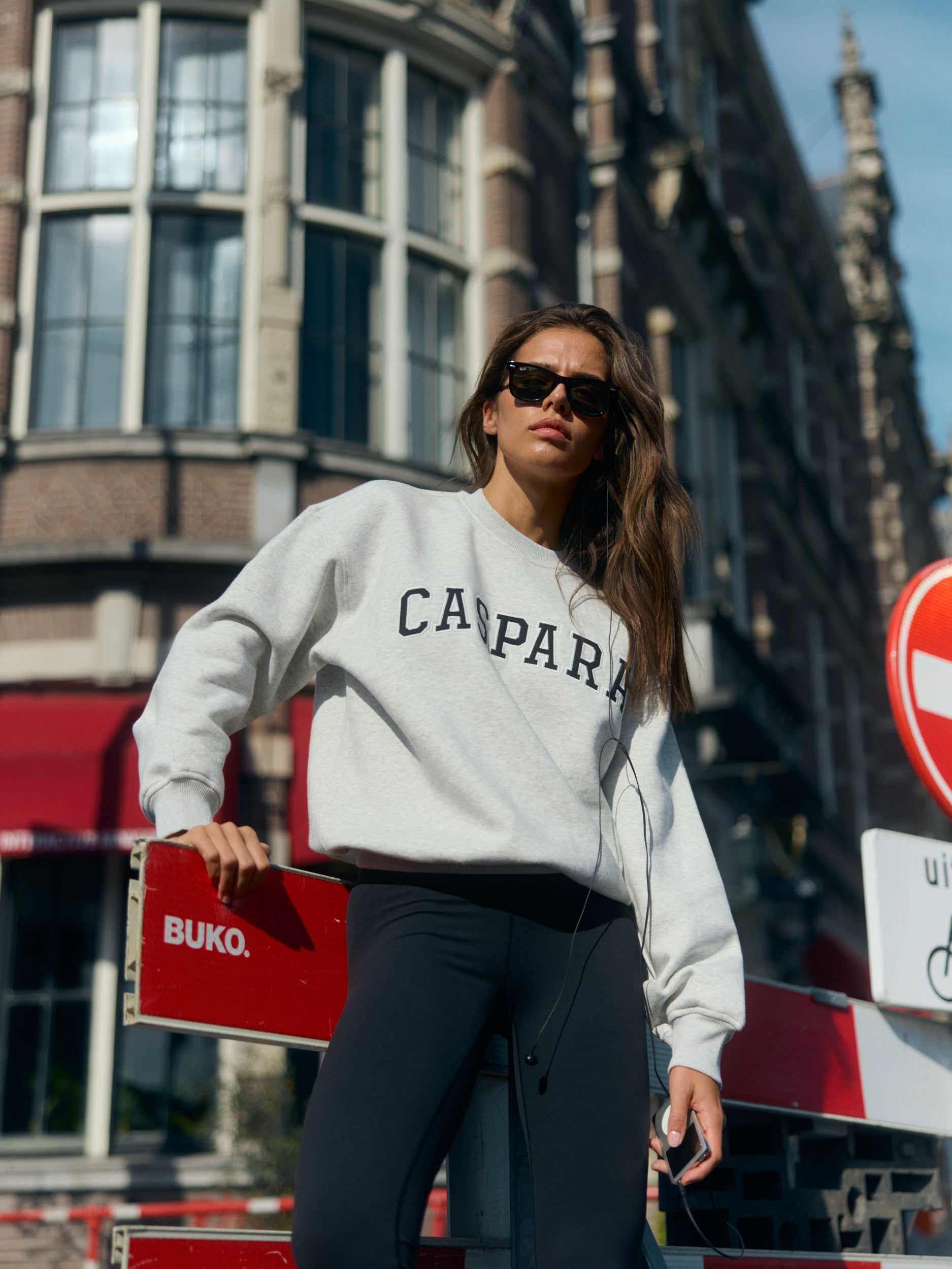 Woman wearing a grey melange CASPARA crewneck sweatshirt and sunglasses on a city street.