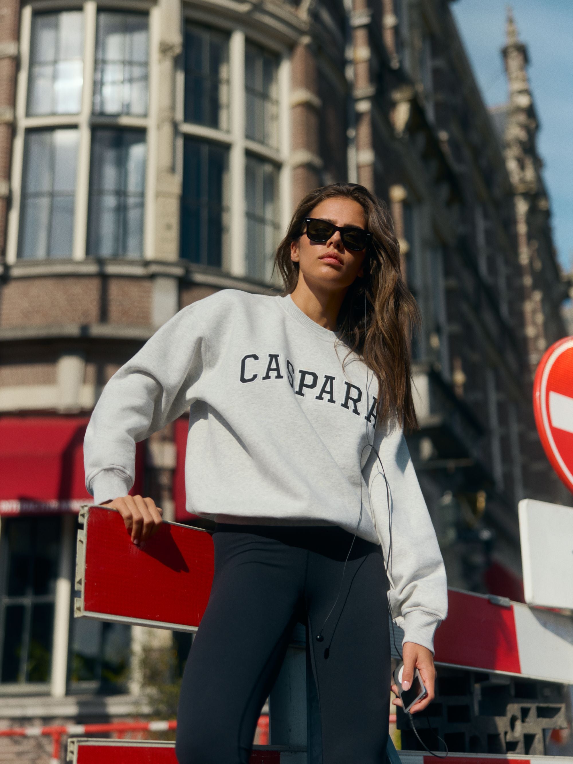 Woman wearing a grey melange CASPARA crewneck sweatshirt and sunglasses in a city setting.