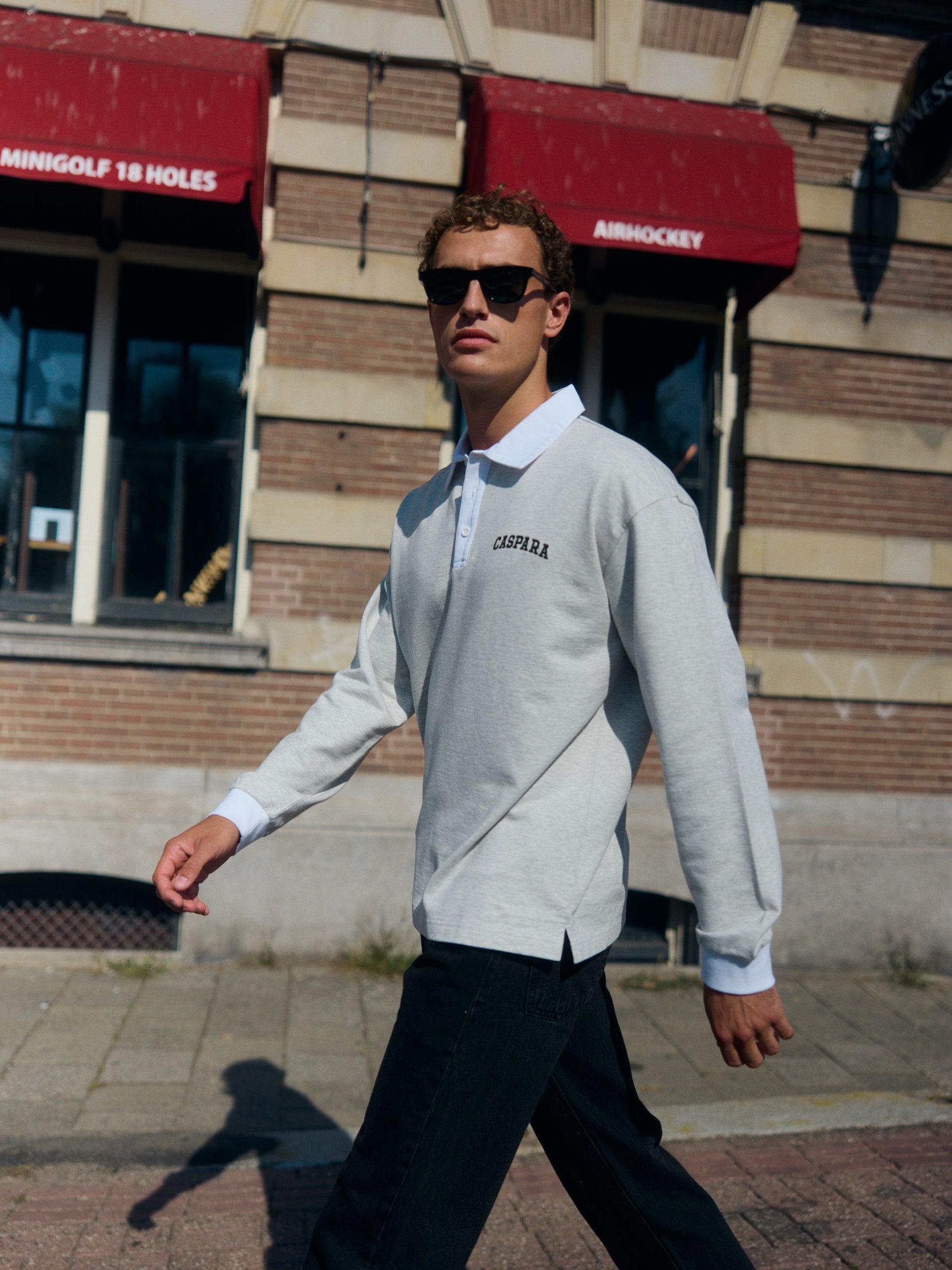 Man wearing a grey long-sleeve rugby shirt with a white collar walking on a city street.