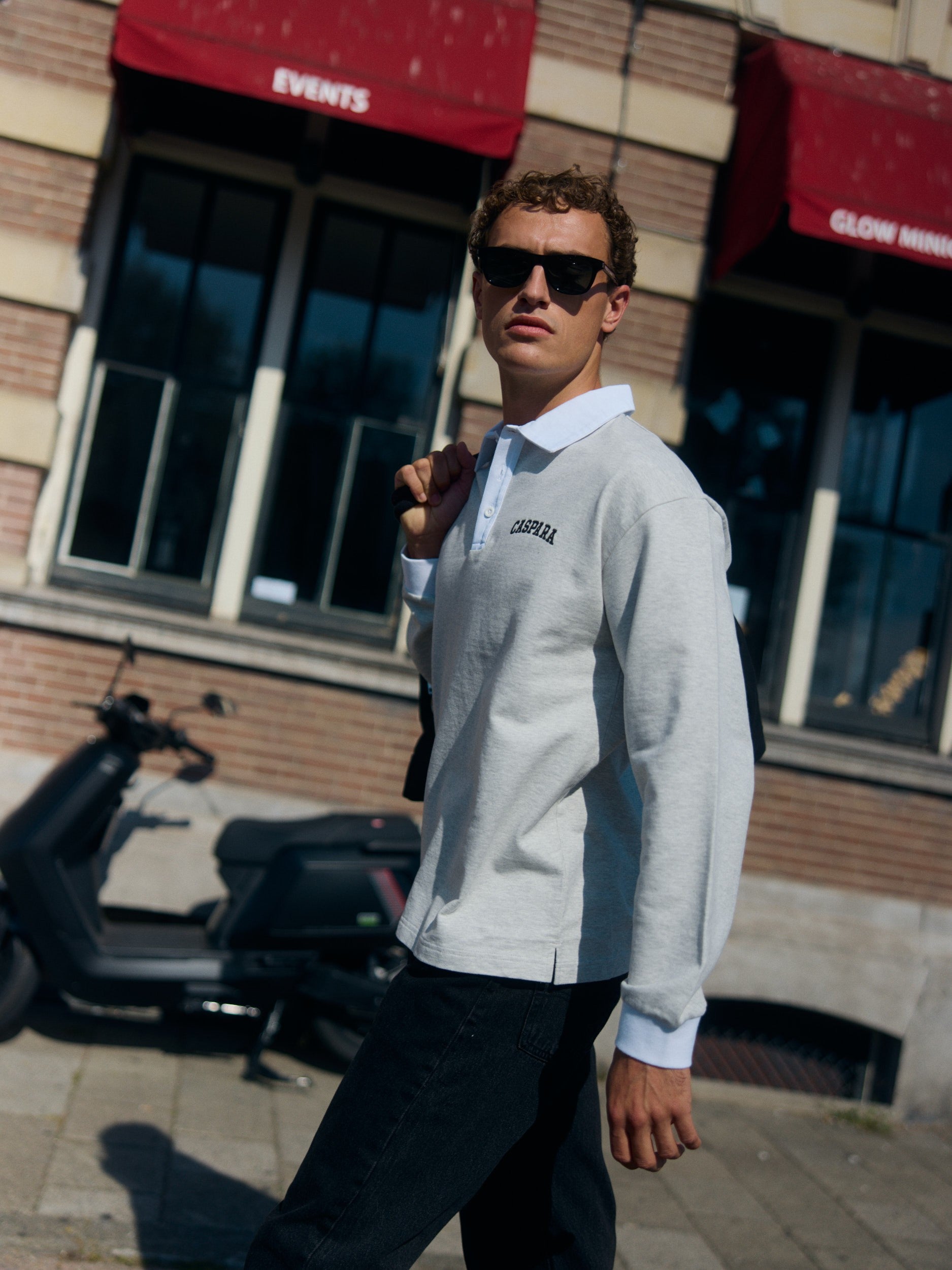 Man wearing a grey long-sleeve rugby shirt with a white collar walking on a city street.