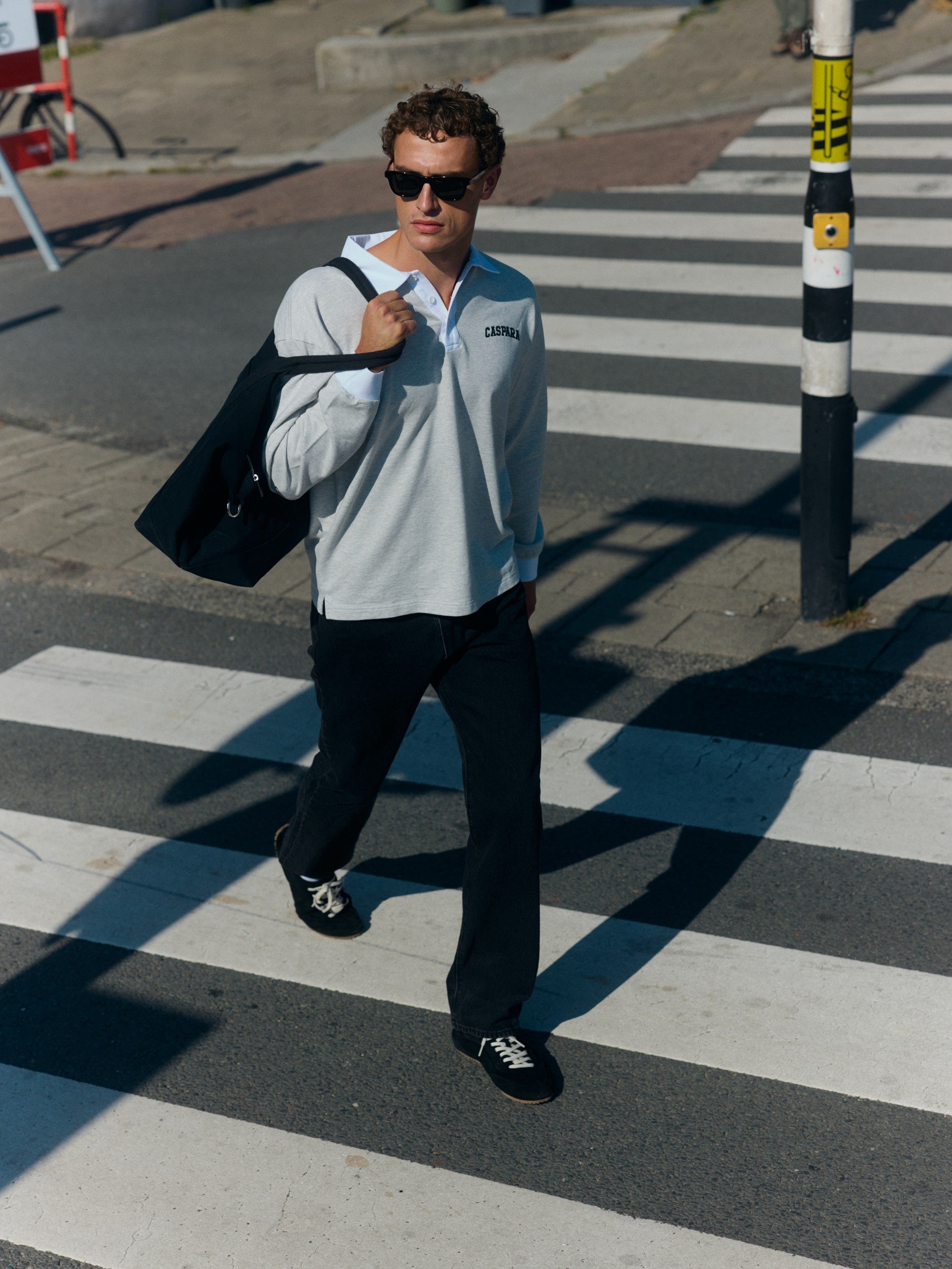 Man wearing a grey long-sleeve rugby shirt with a white collar walking across a crosswalk.