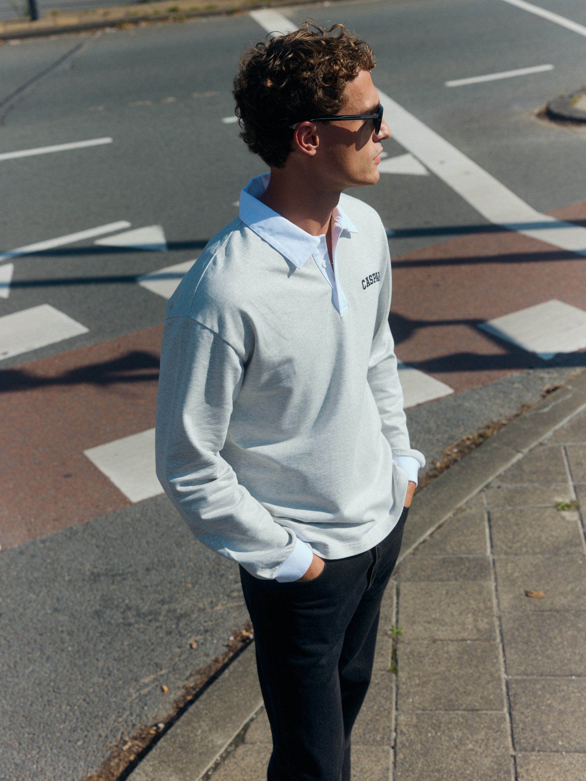 Man wearing a light grey cotton rugby shirt with a white collar on a city street.