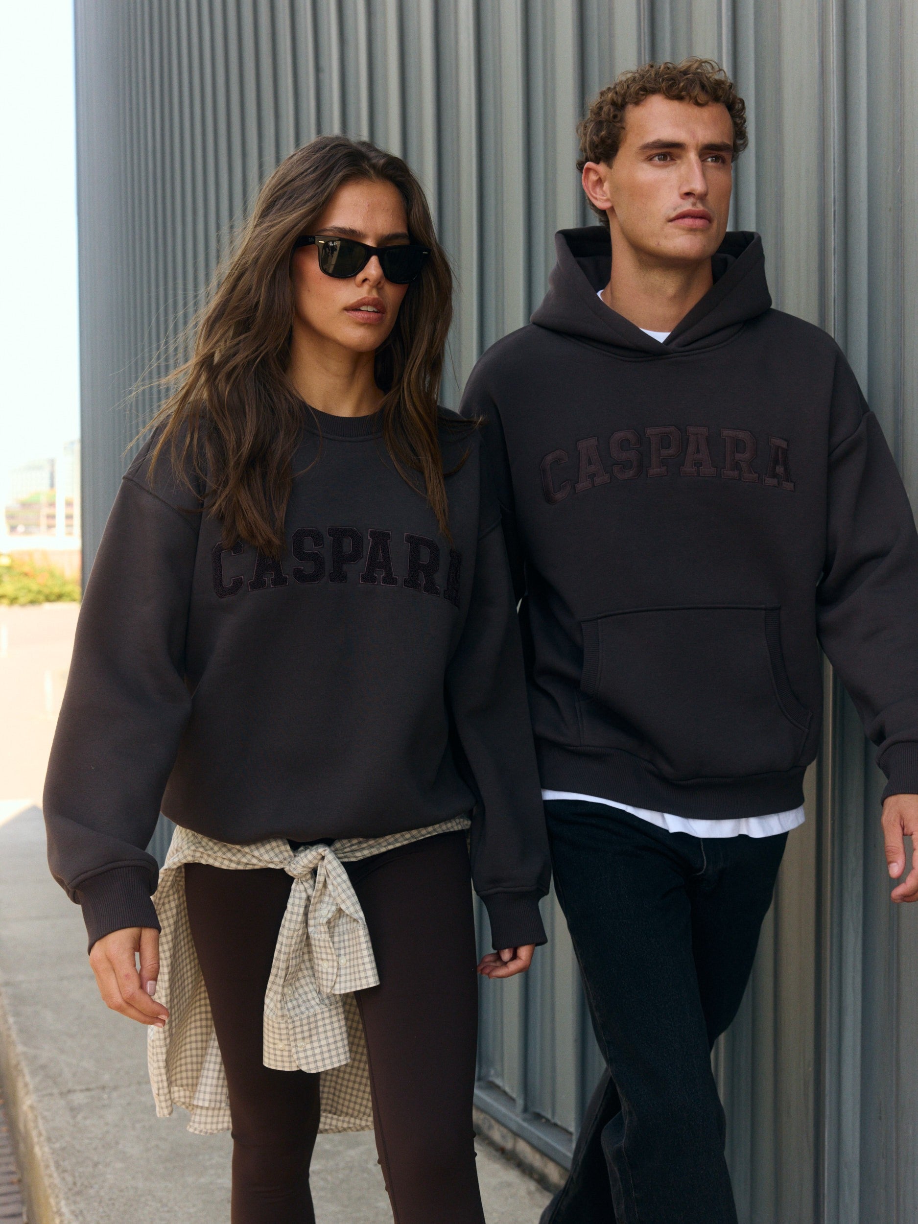 Woman wearing an espresso brown CASPARA crewneck sweatshirt walking outdoors alongside a man in a hoodie.