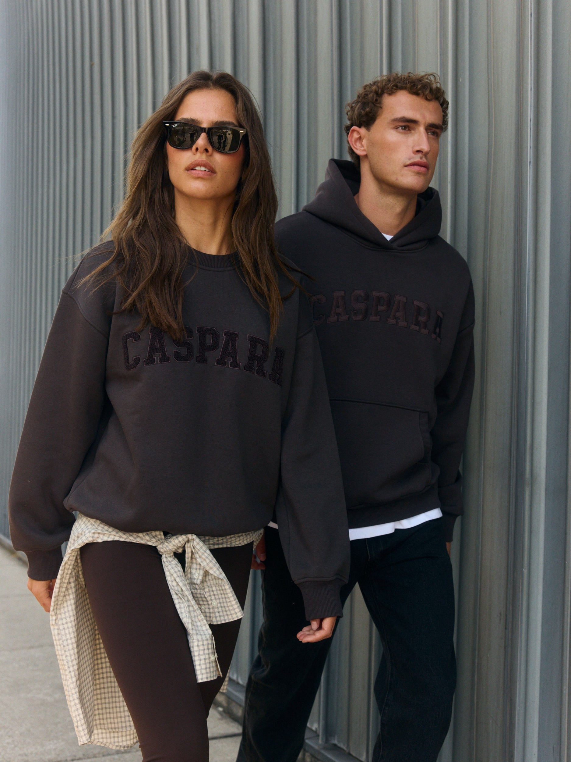 Woman wearing an espresso brown CASPARA crewneck sweatshirt walking alongside a man in a hoodie.