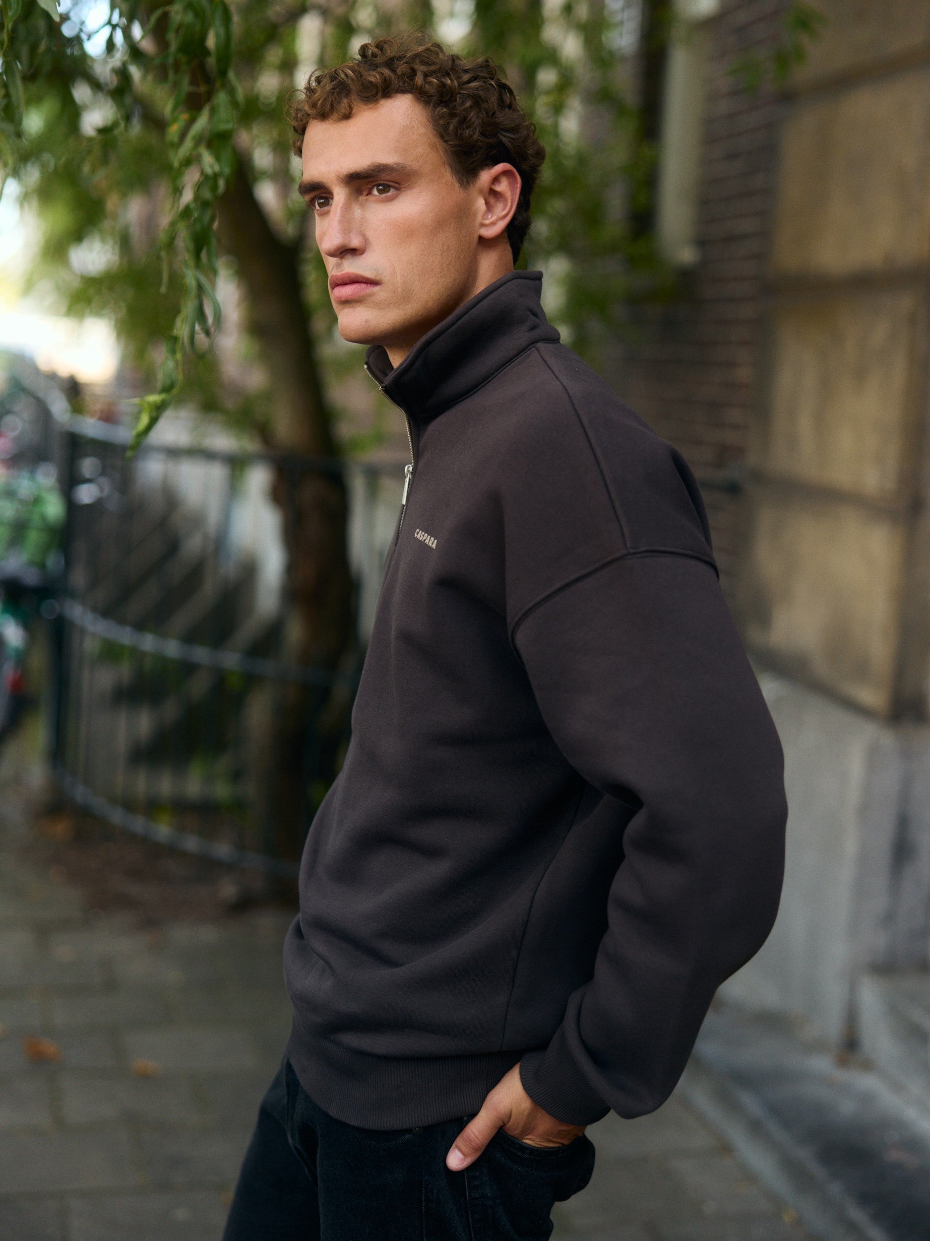 Man wearing an espresso brown quarter-zip sweatshirt standing on a city sidewalk.