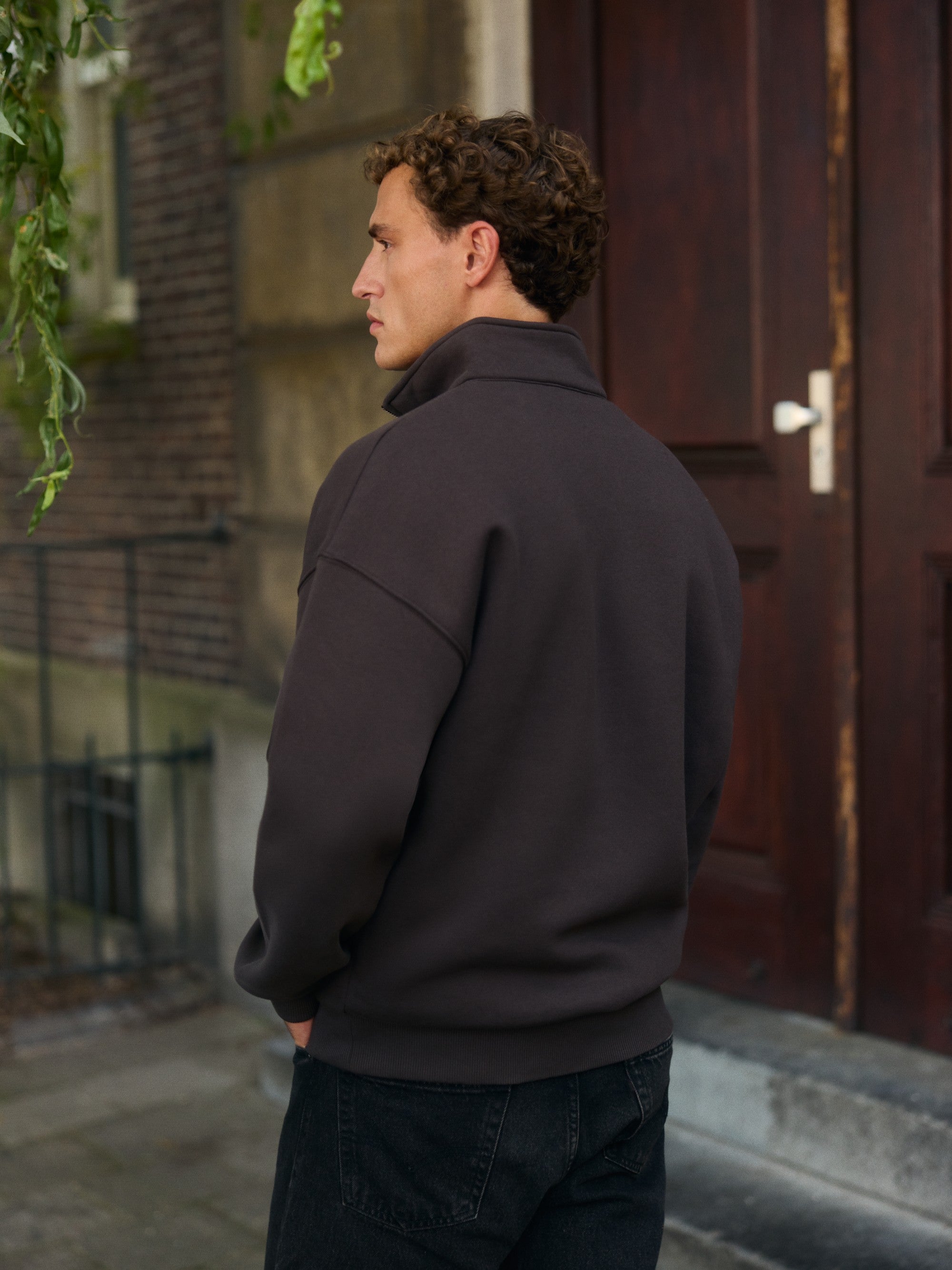 Man wearing an espresso CASPARA 1/4 zip sweatshirt standing outside an entrance.