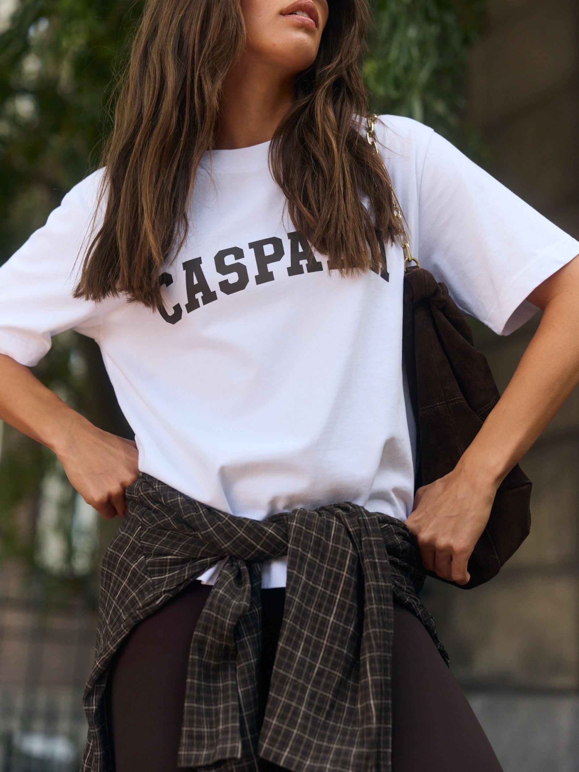 Woman wearing a white Caspara graphic t-shirt with a plaid shirt tied around her waist.