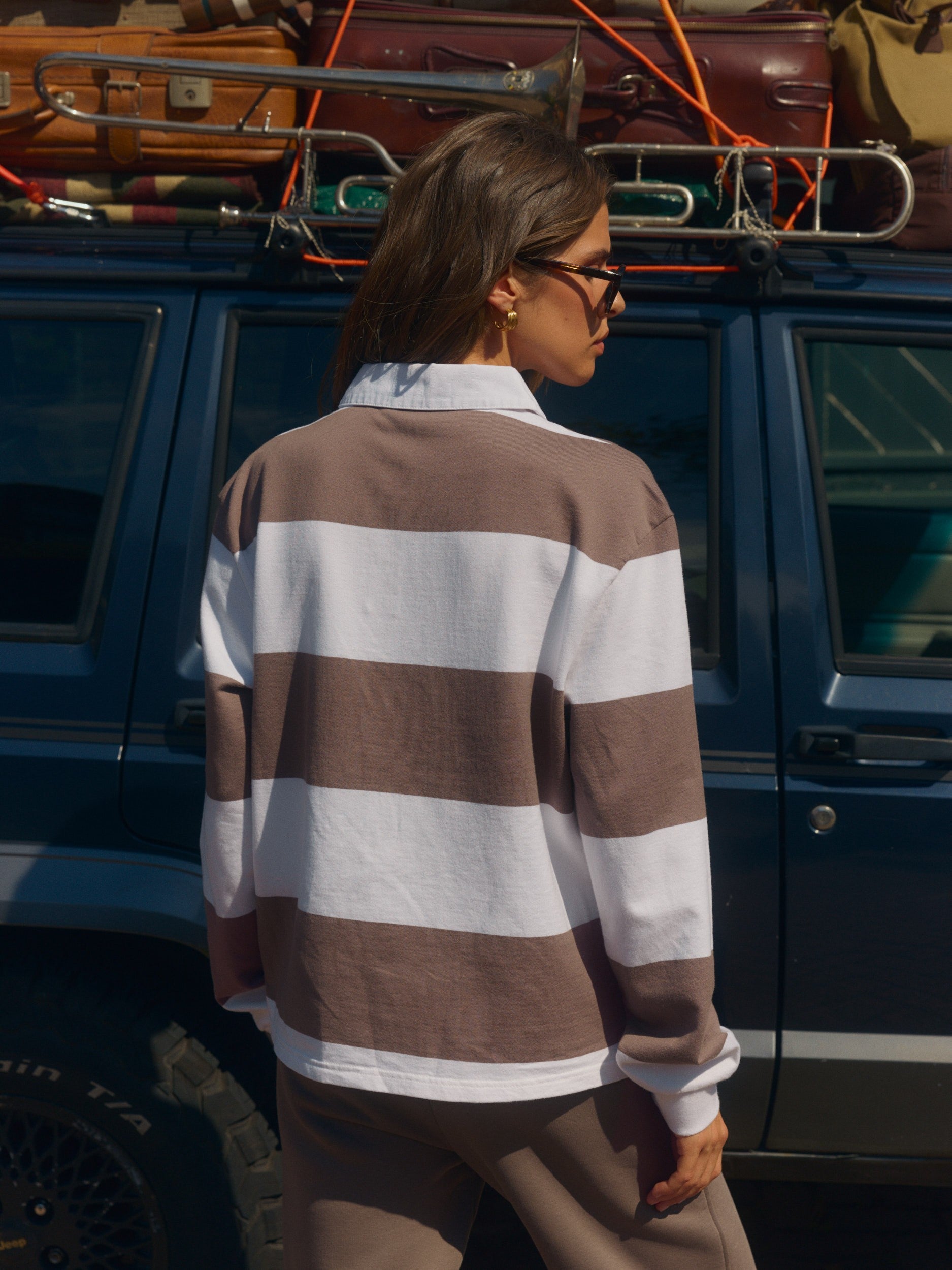 Woman wearing a walnut and white striped long-sleeve rugby shirt beside a car.