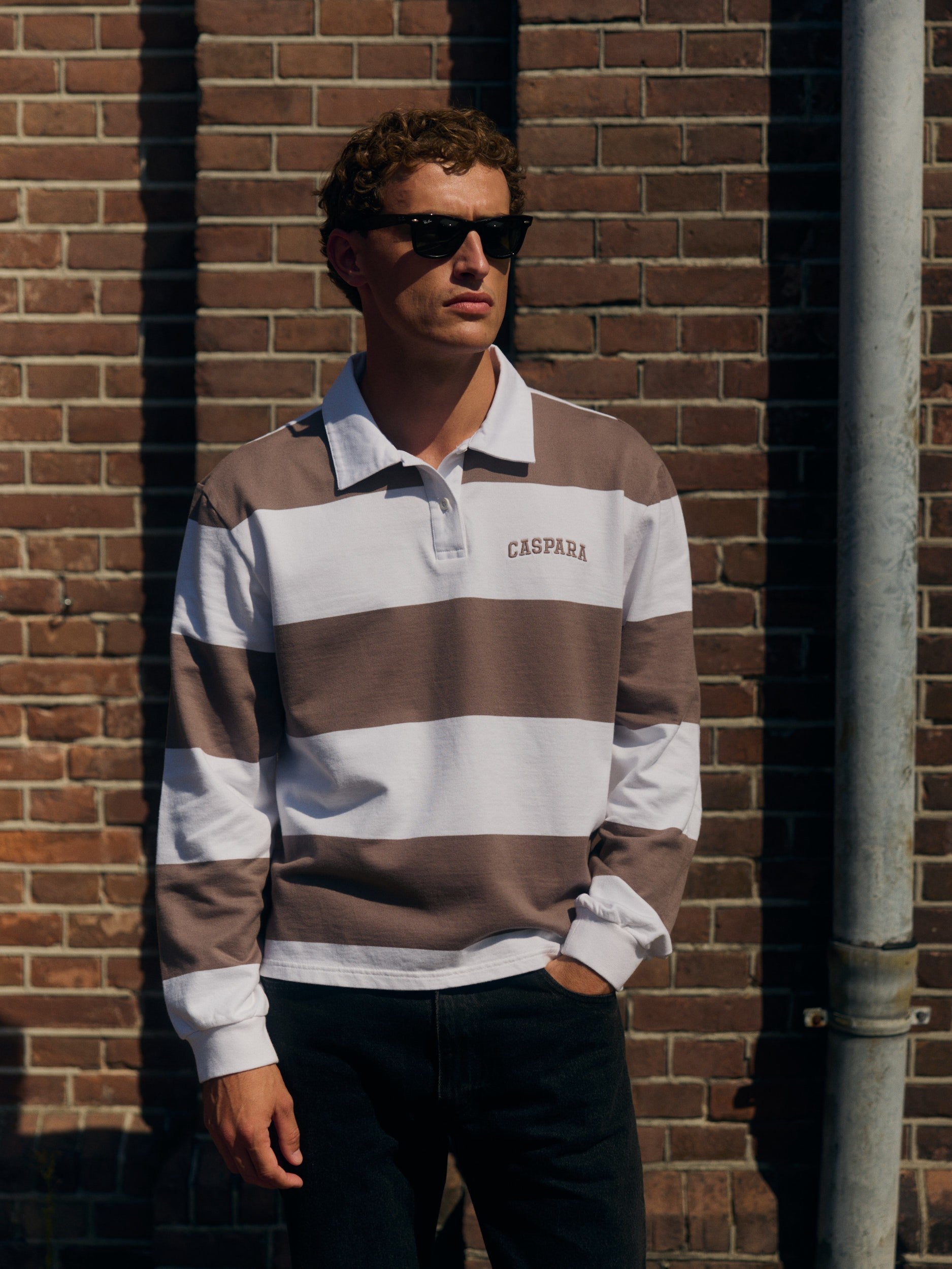 Man wearing a walnut and white striped long-sleeve rugby shirt against a brick wall.