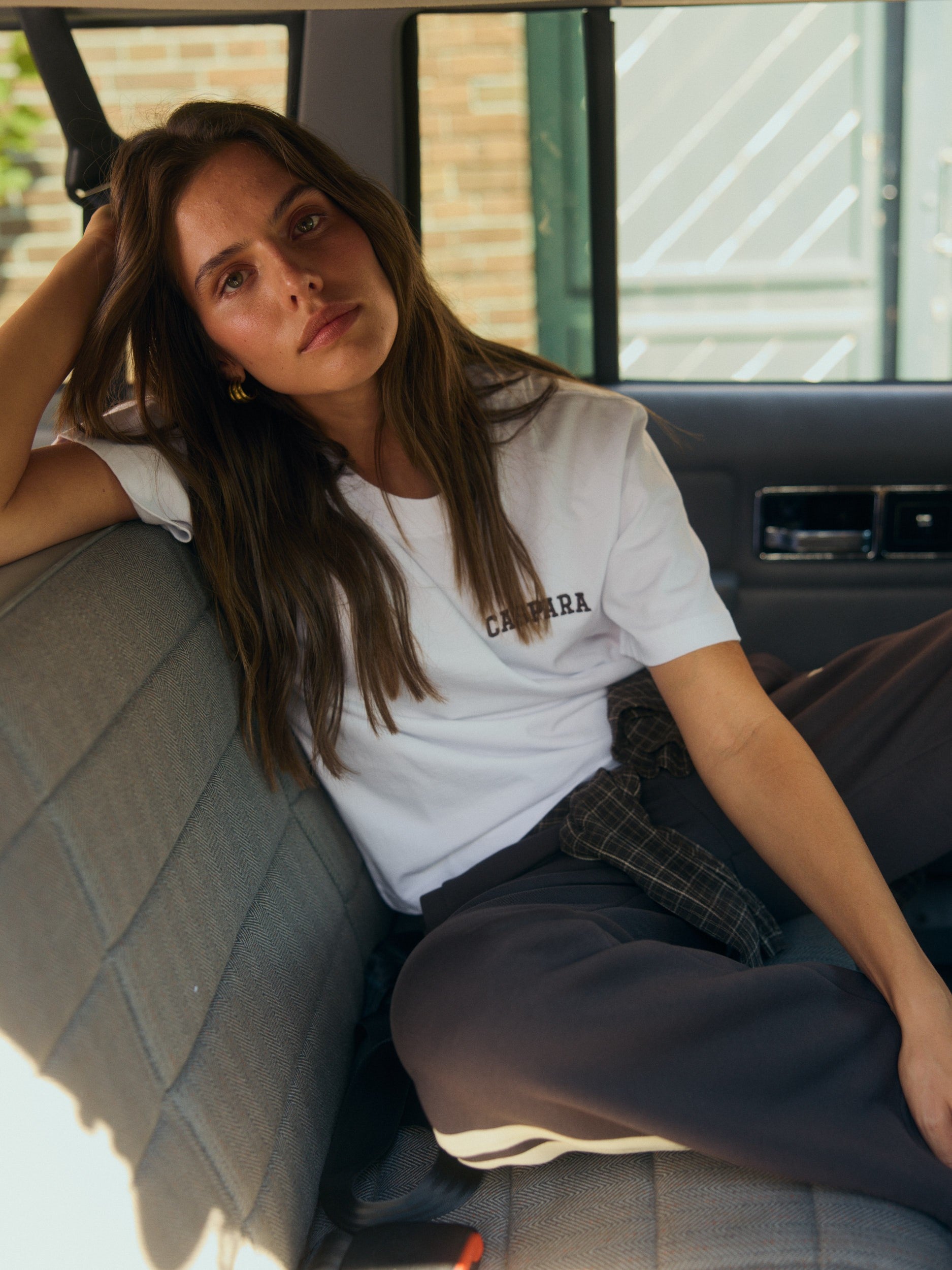 Woman wearing a white embroidered CASPARA t-shirt sitting in the back seat of a vintage car.