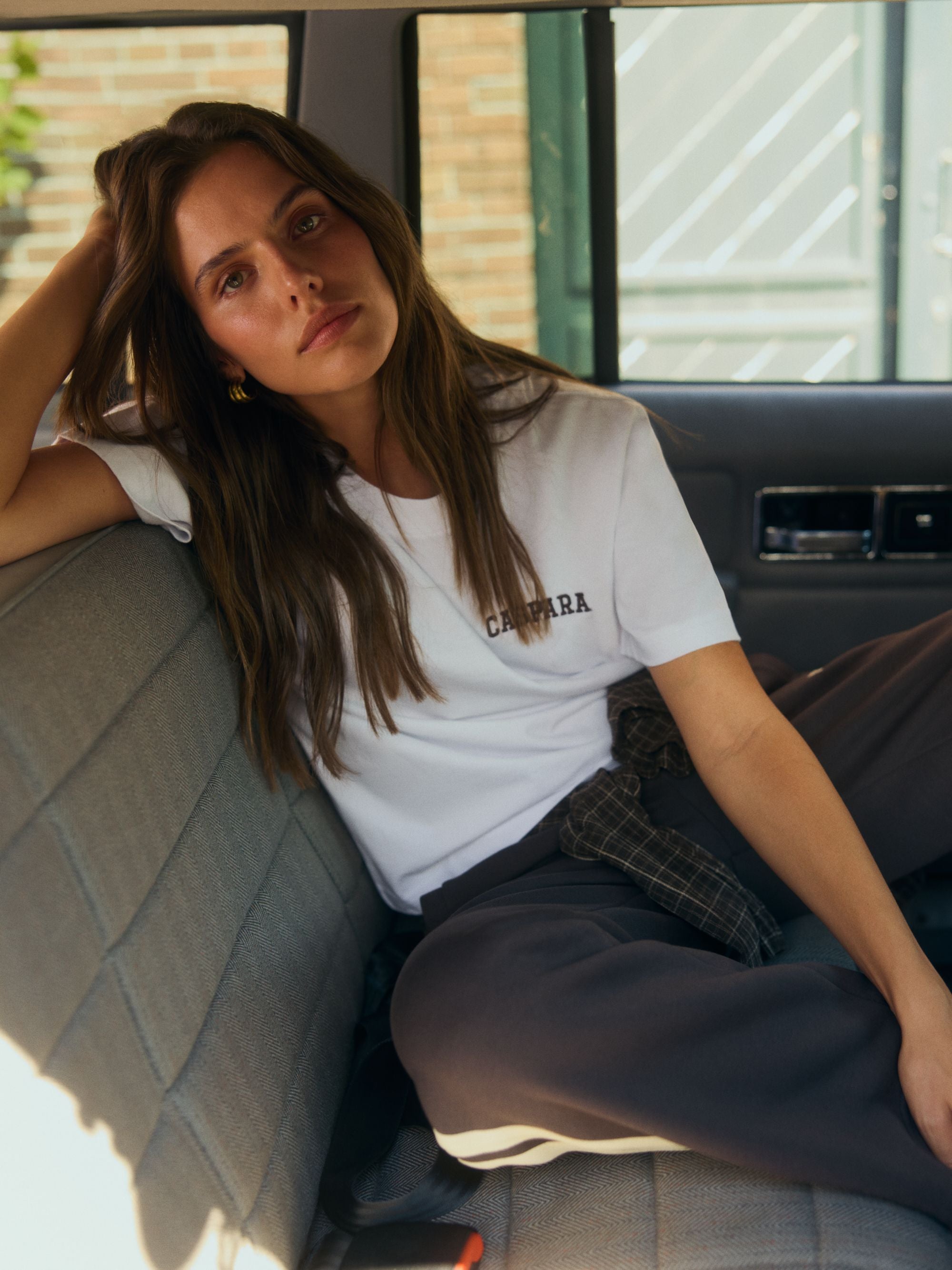 Woman wearing a white CASPARA embroidered t-shirt sitting in the back seat of a car.