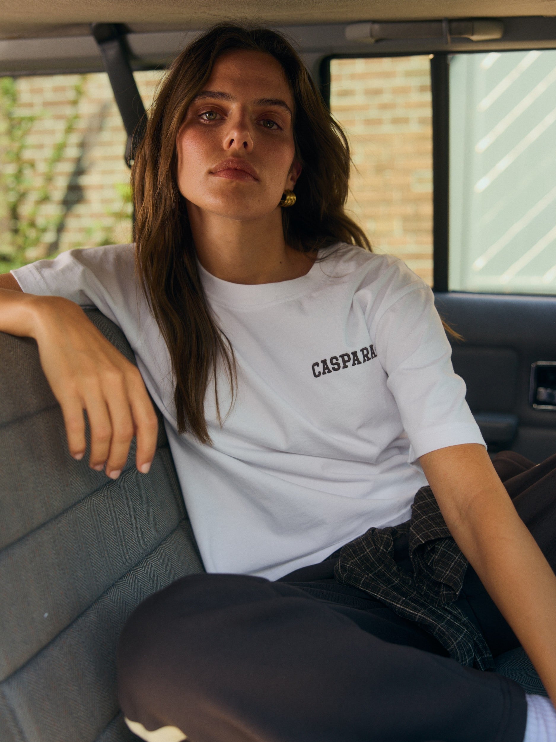 Woman wearing a white Caspara embroidered t-shirt sitting in the back seat of a car.