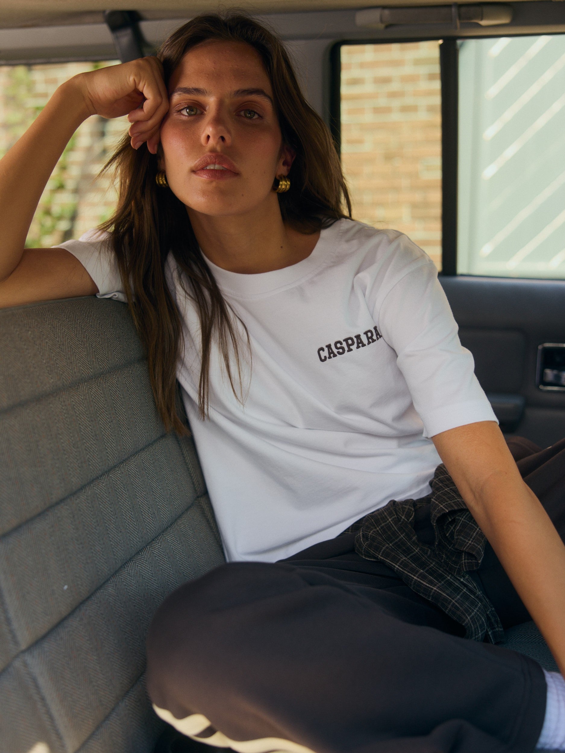 Woman wearing a white oversized embroidered t-shirt sitting in the back of a car.