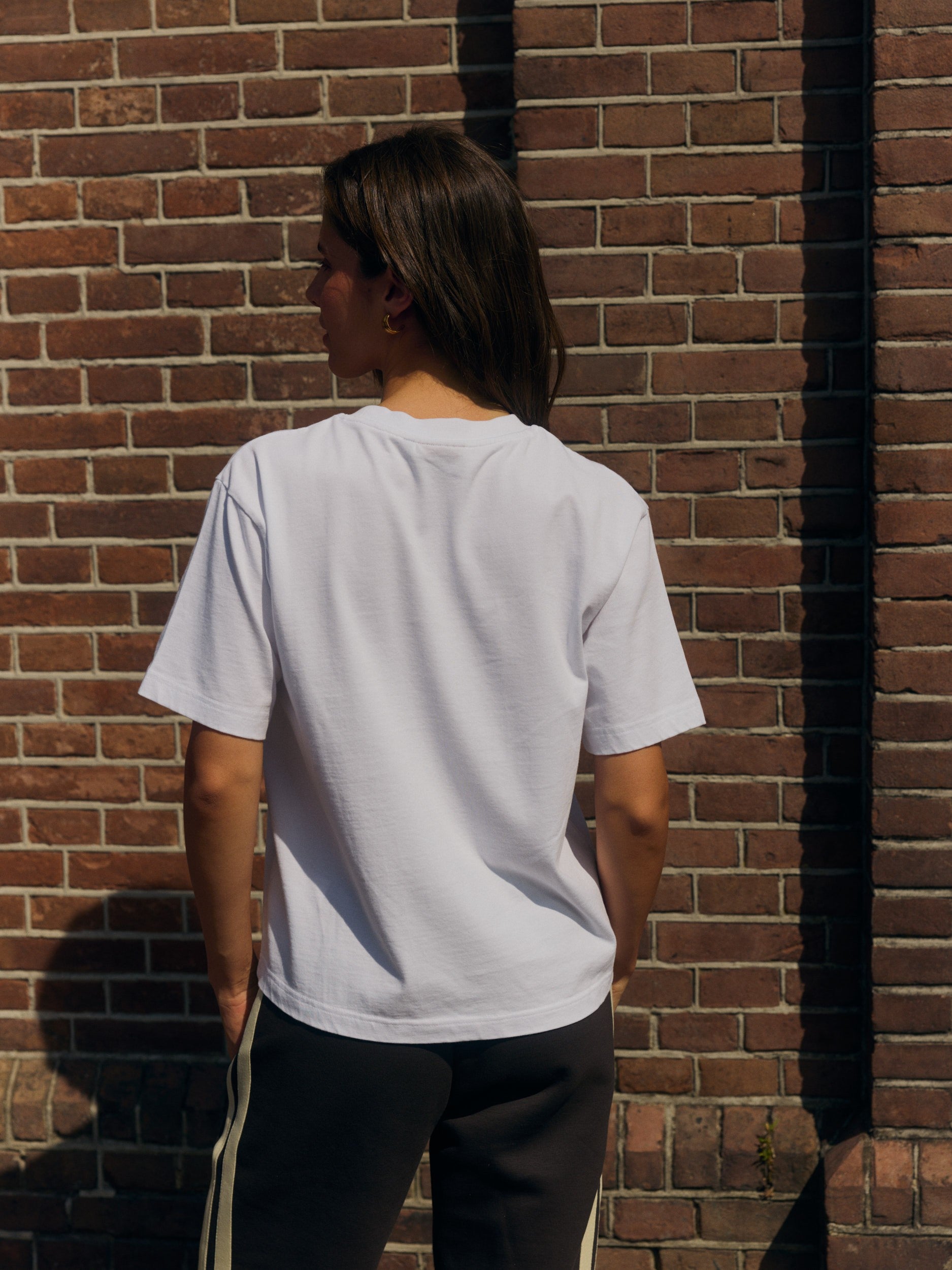 Back view of a woman wearing a white oversized cotton t-shirt against a brick wall.