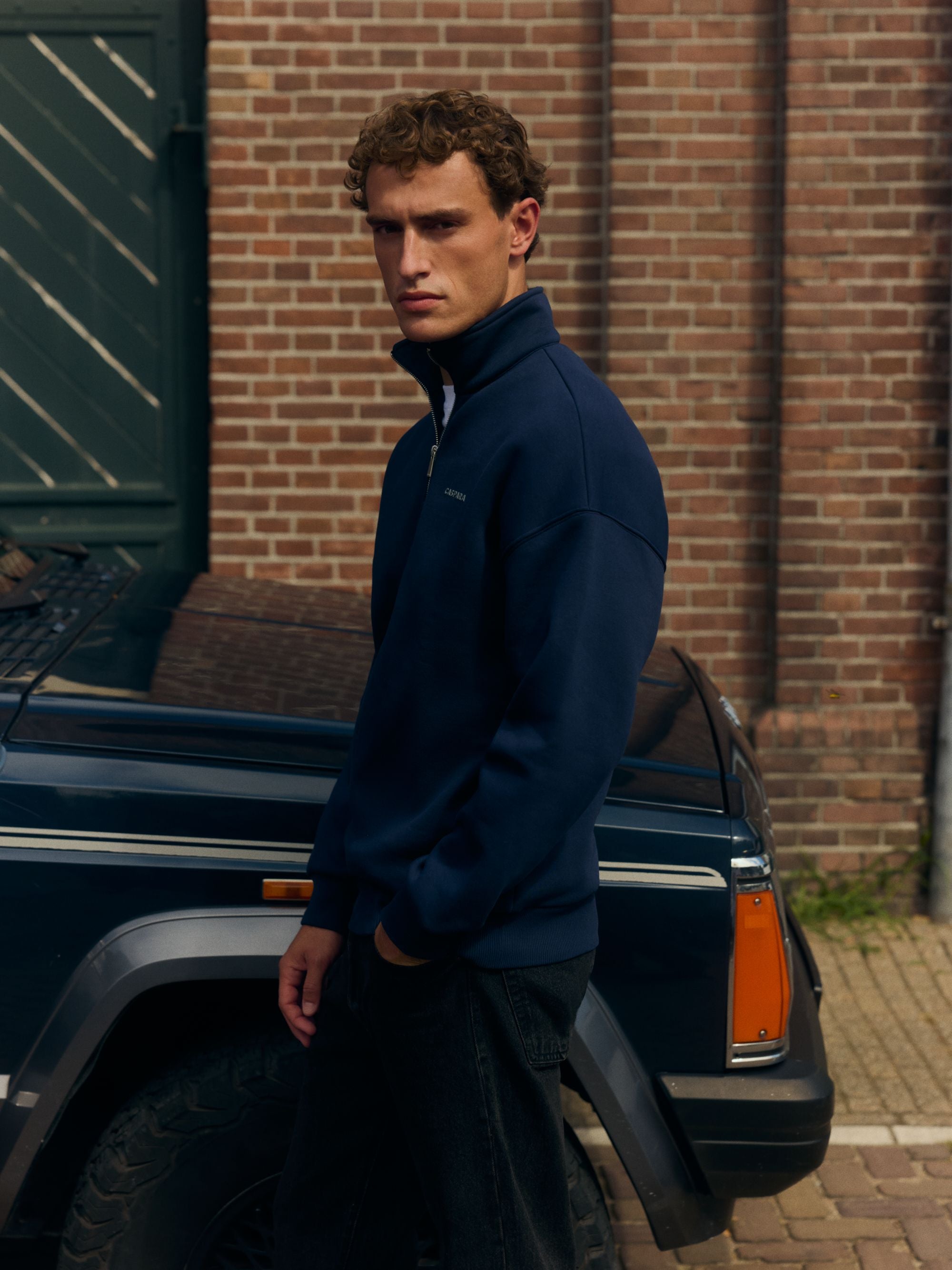 Man wearing a navy CASPARA quarter-zip sweatshirt standing outside next to a car.