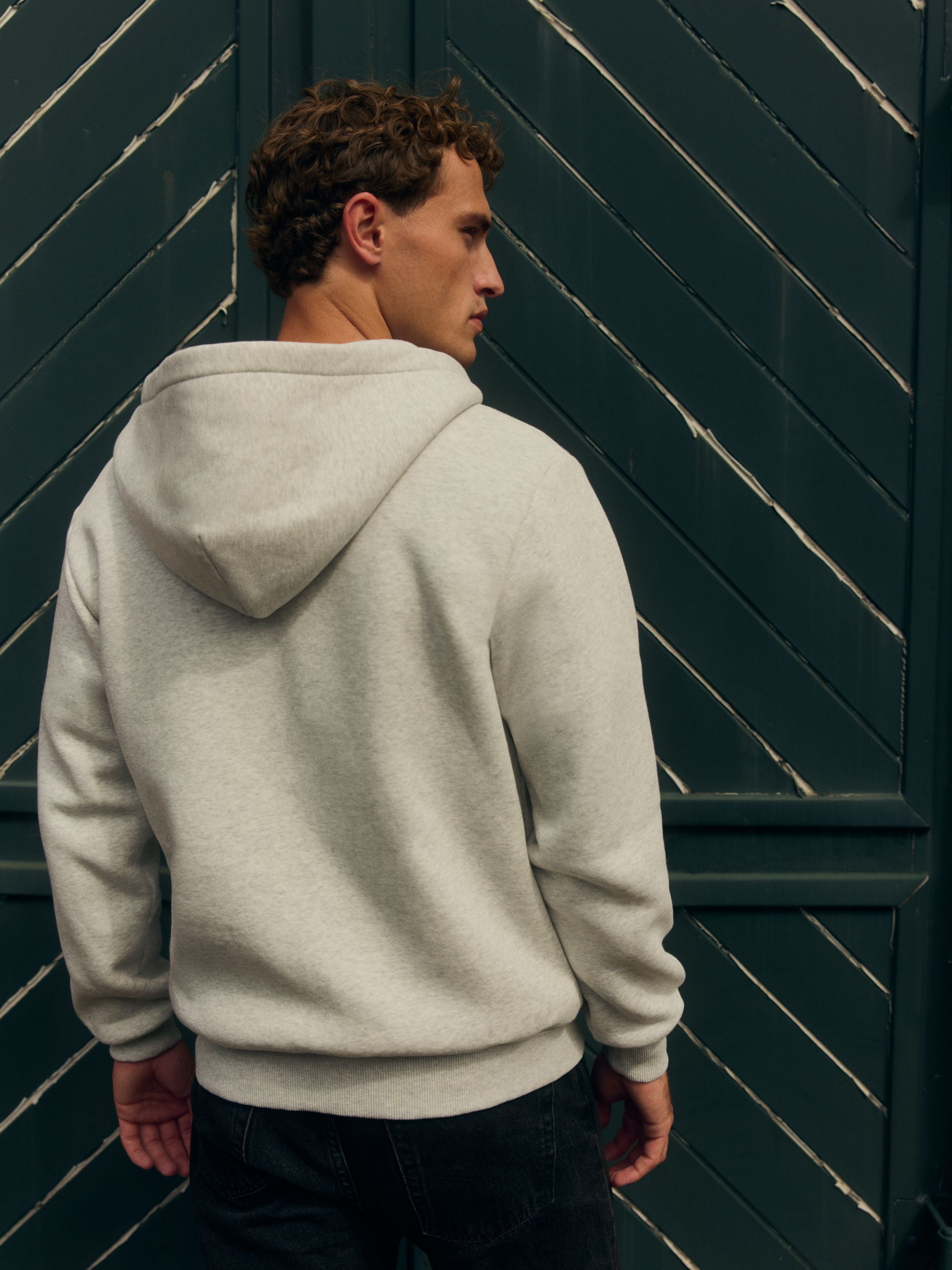 Man from behind wearing a grey melange CASPARA hoodie against a dark green door.