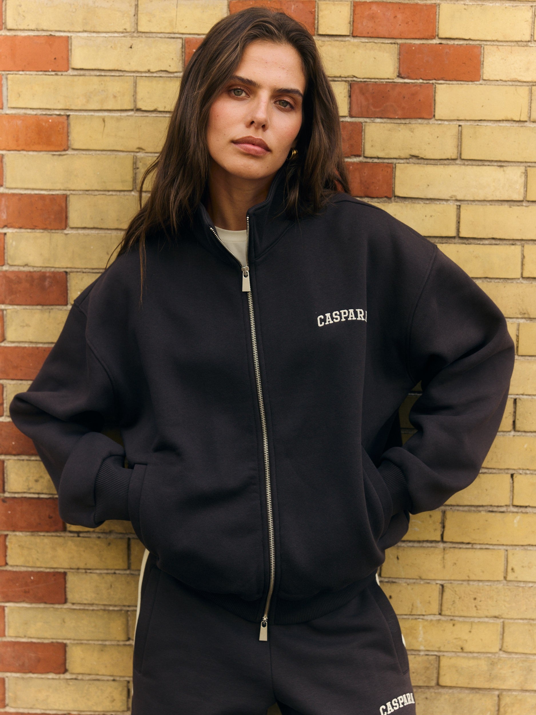 Woman wearing an espresso brown funnel neck zip jacket against a brick wall.