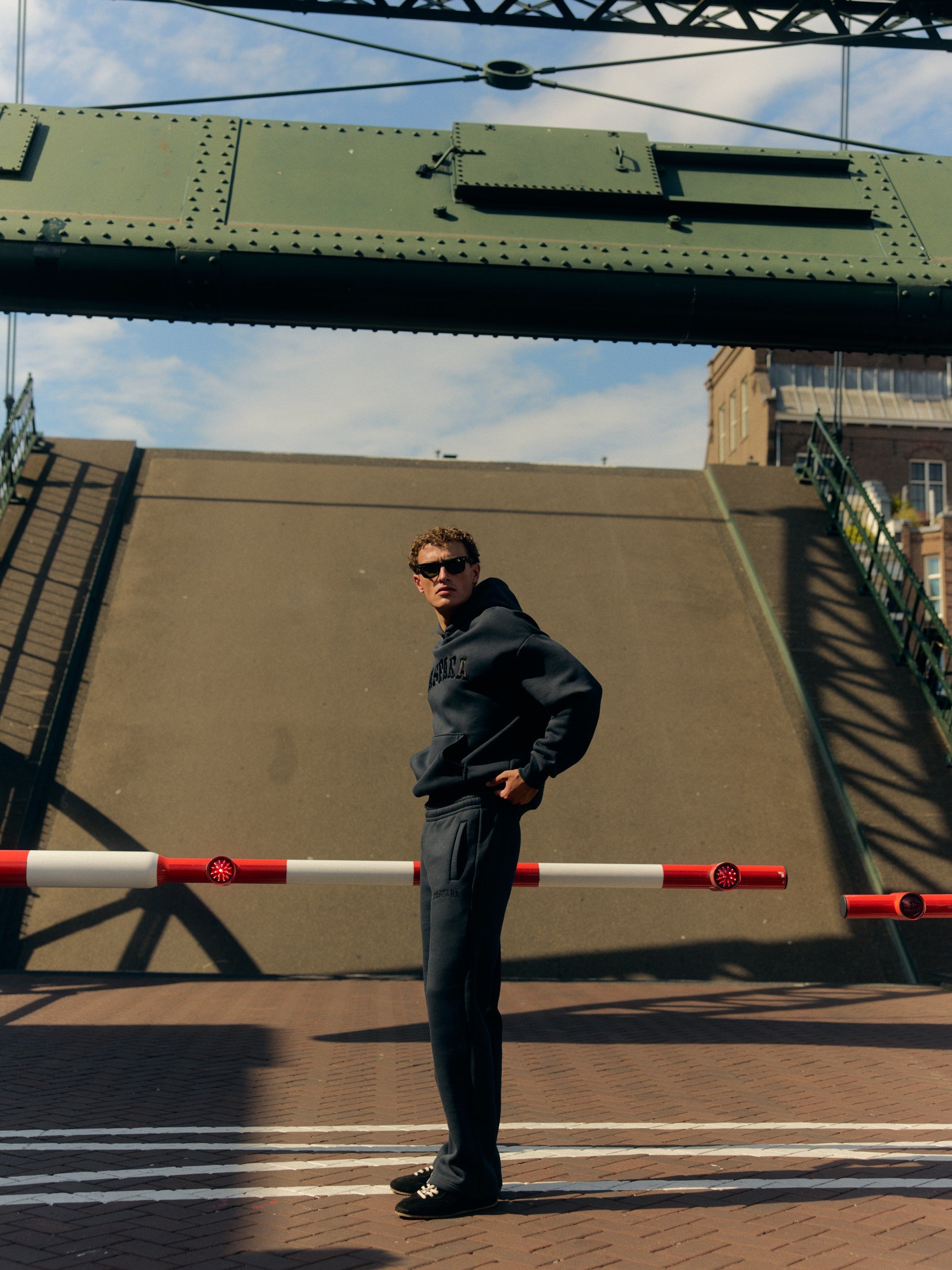 Man wearing a dark navy hoodie and straight-leg sweatpants standing on a raised drawbridge.