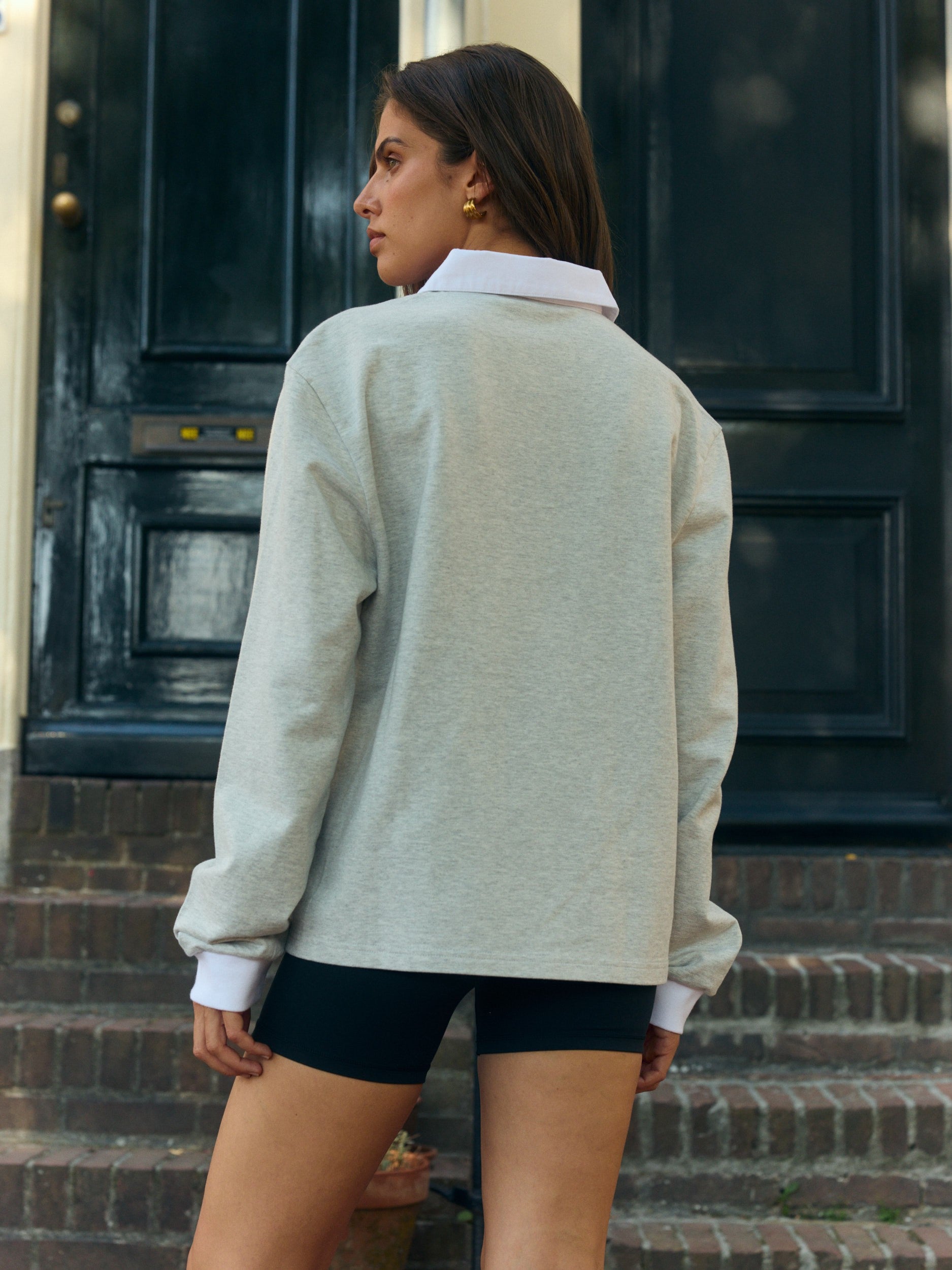 Woman wearing a light grey rugby shirt with a white collar standing on steps in front of a dark door.