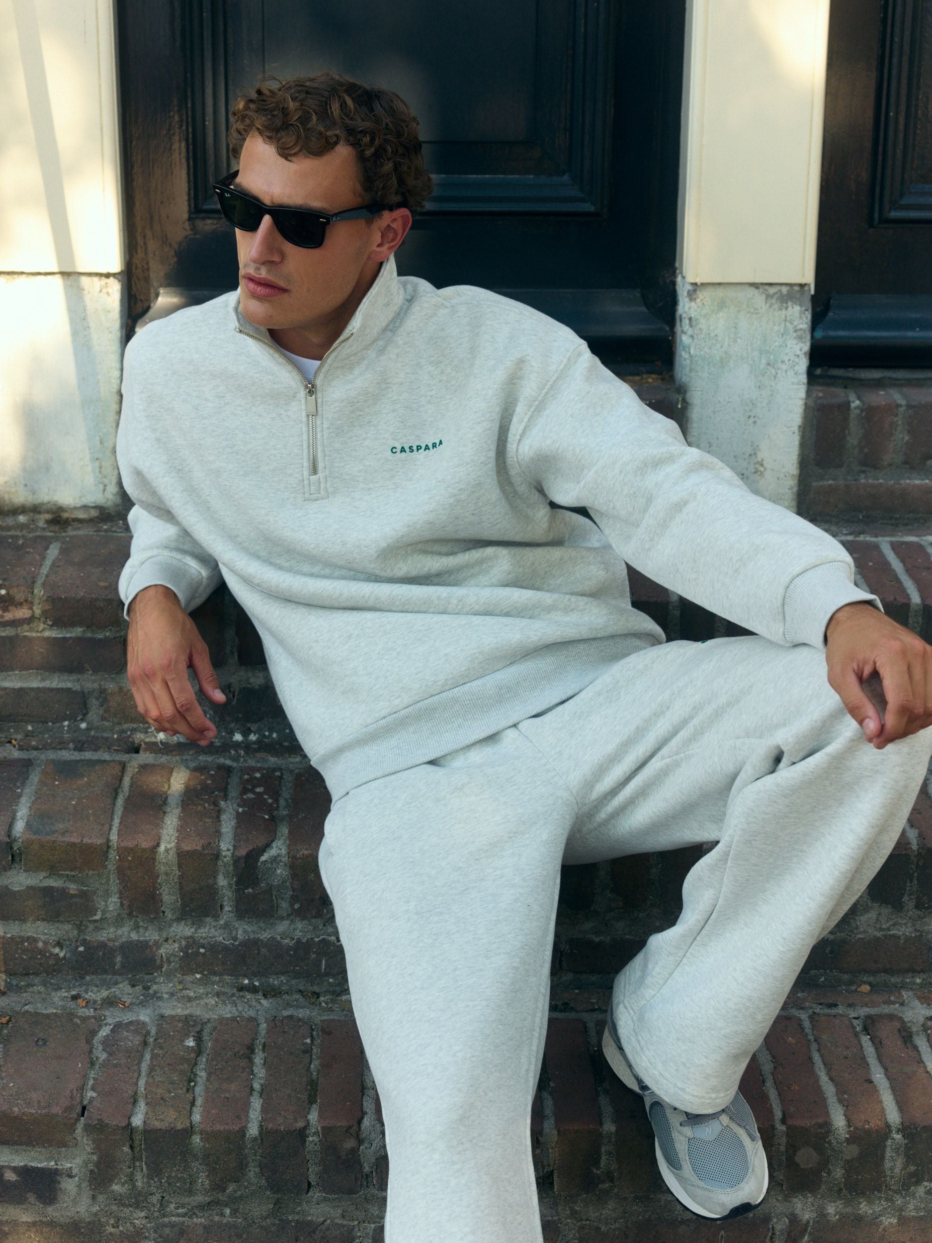 Man wearing a grey melange 1/4 zip sweatshirt and matching sweatpants sitting on brick steps.