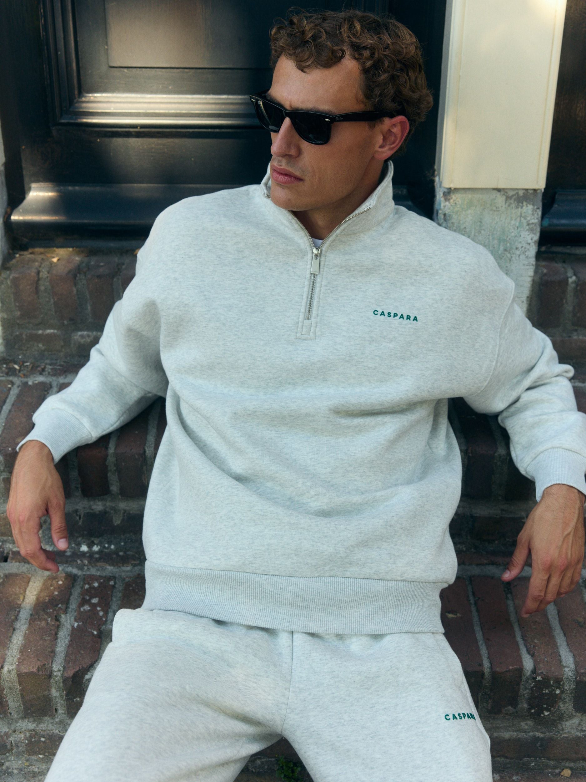Man wearing a grey melange quarter-zip sweatshirt and sunglasses sitting on brick steps.