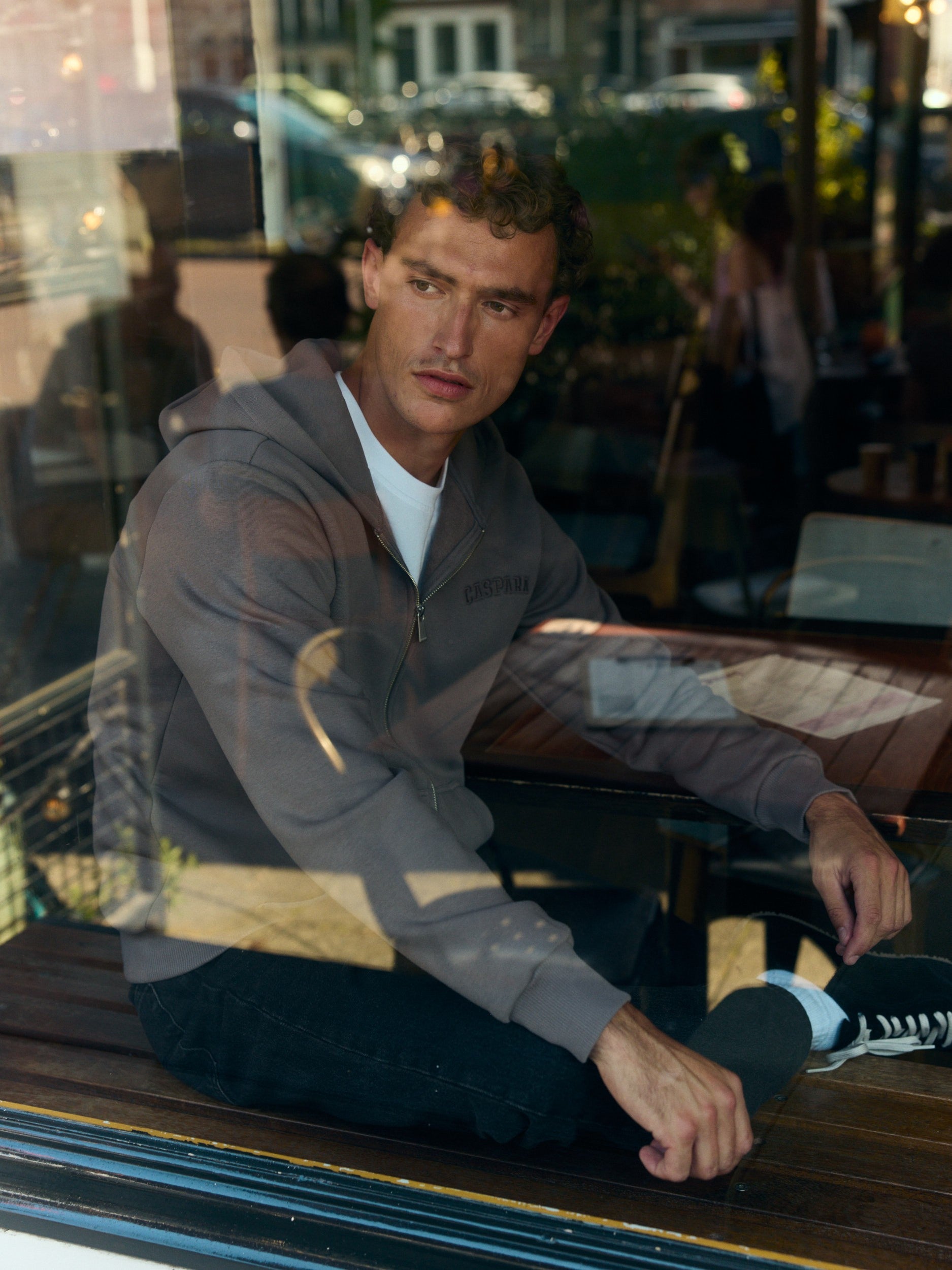 Man wearing a walnut zip-up hoodie sitting by a cafe window.