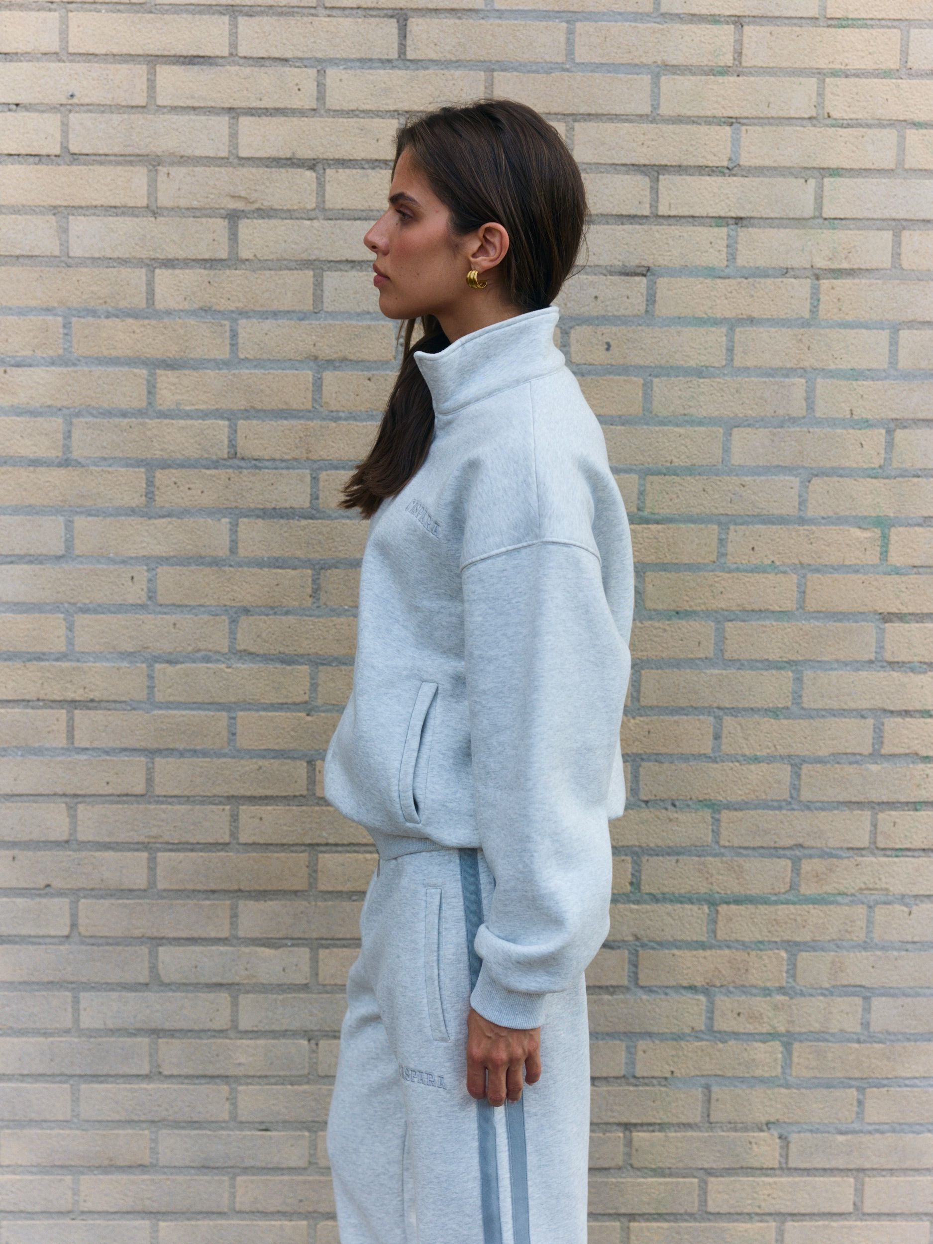 Woman wearing a grey melange funnel-neck zip jacket against a brick wall.