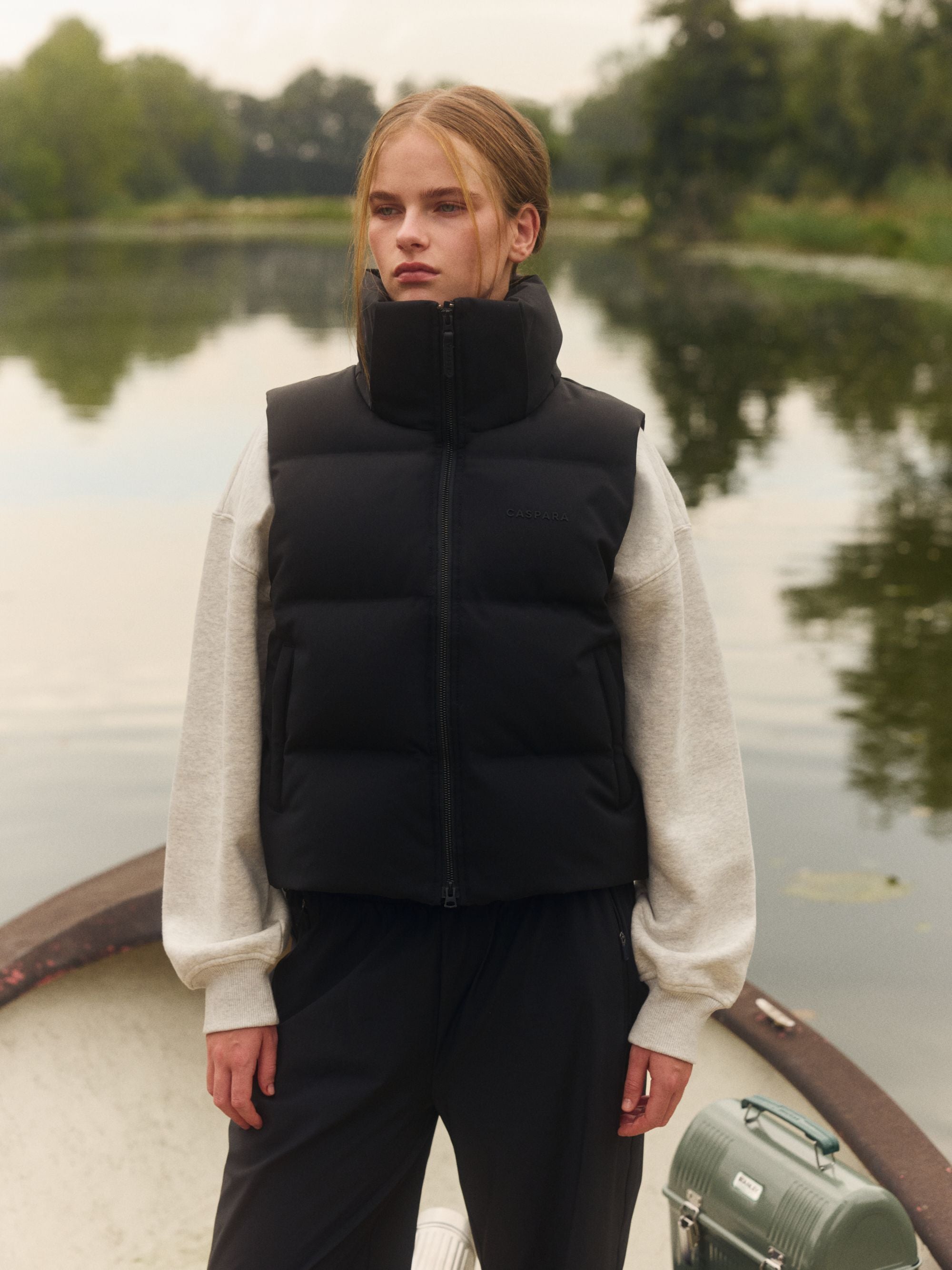 Woman wearing a black CASPARA puffer vest over a grey sweatshirt outdoors on a boat.