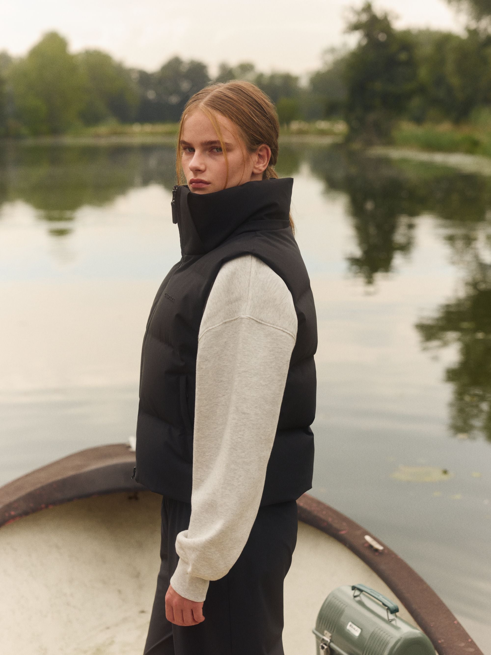 Woman wearing a black CASPARA puffer vest over a grey sweatshirt in a boat on a lake.