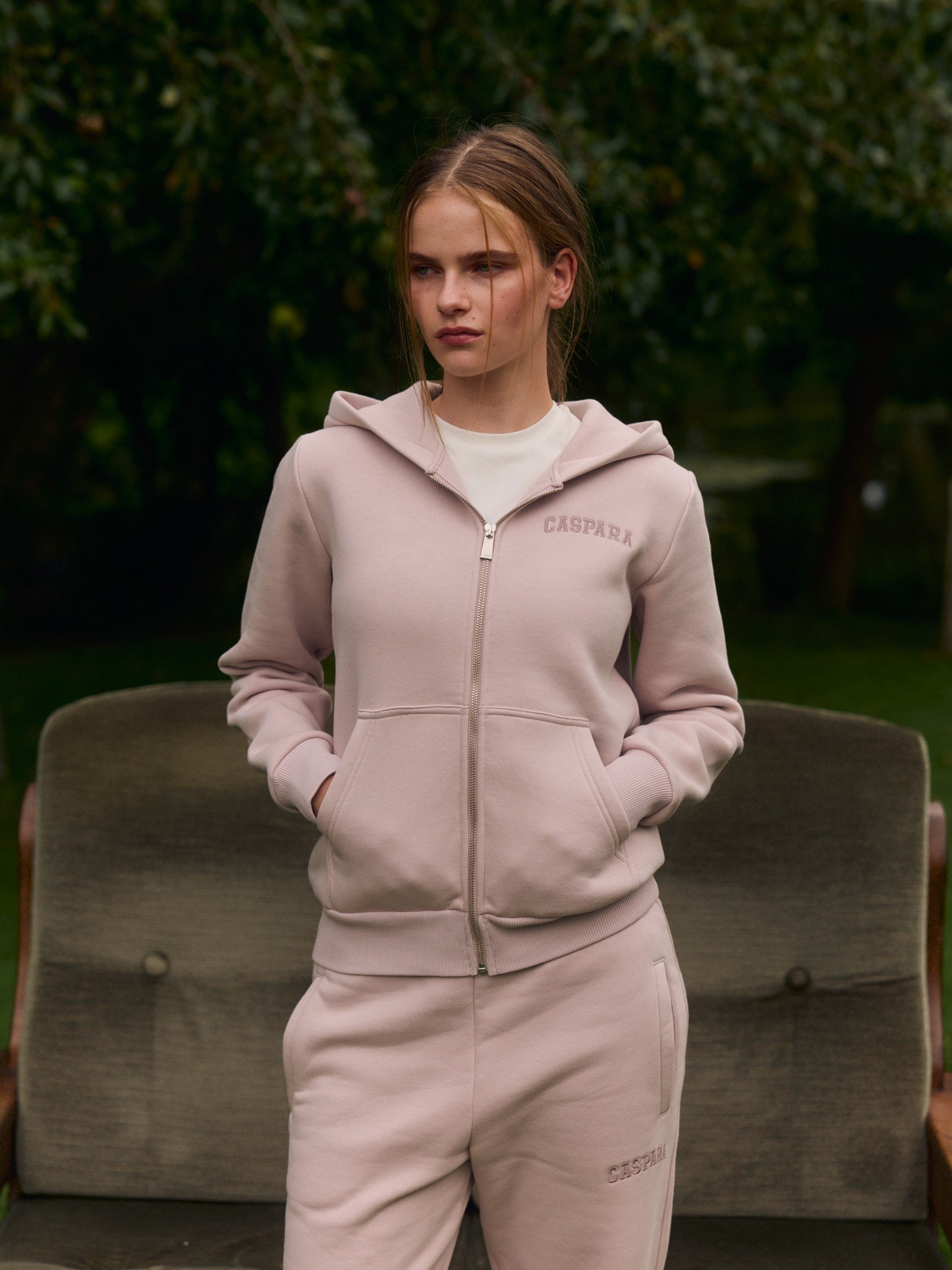 Woman wearing a dusty pink zip hoodie and matching sweatpants in an outdoor garden.