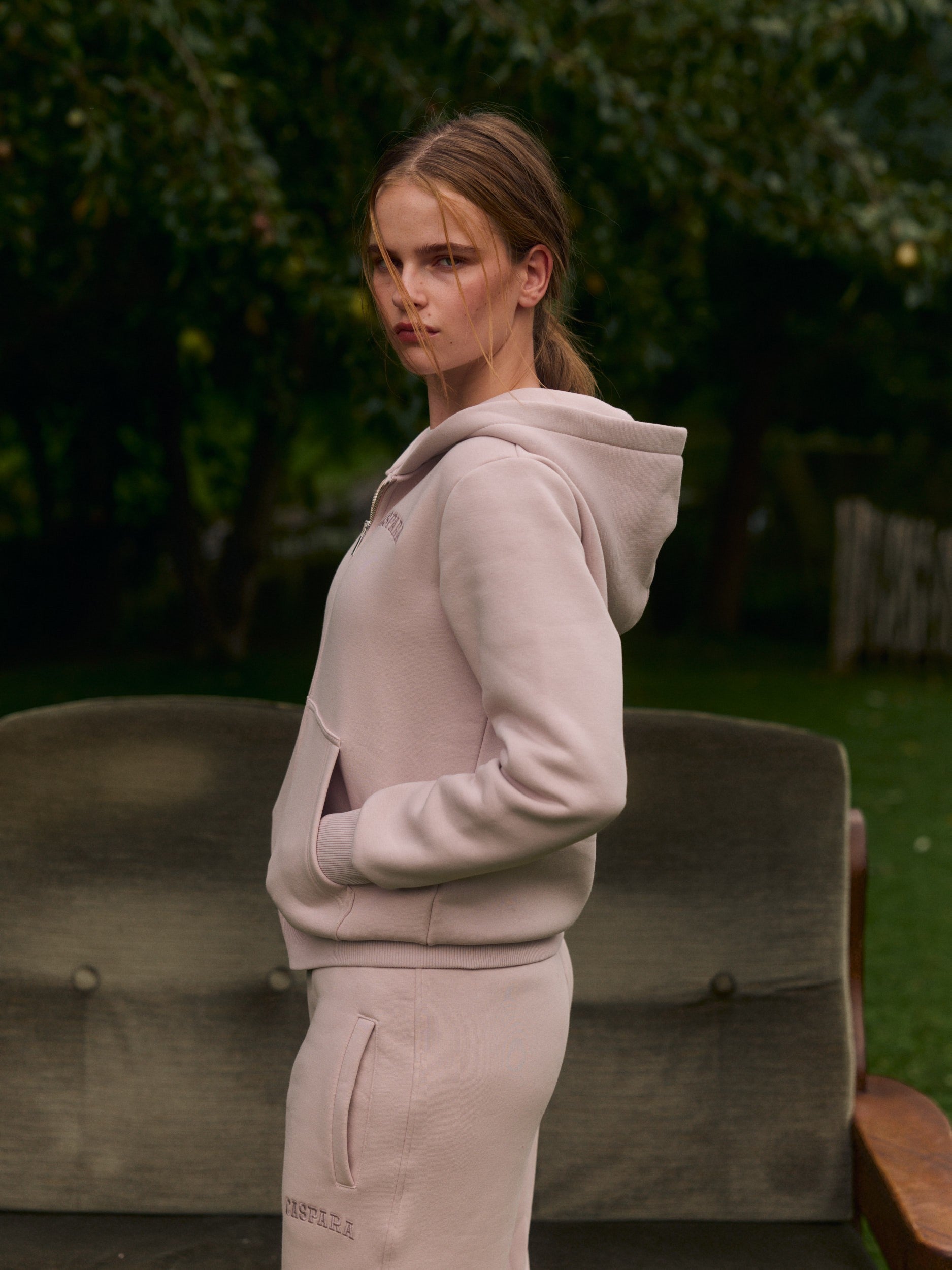 Woman wearing a dusty pink zip-up hoodie with matching sweatpants outdoors.
