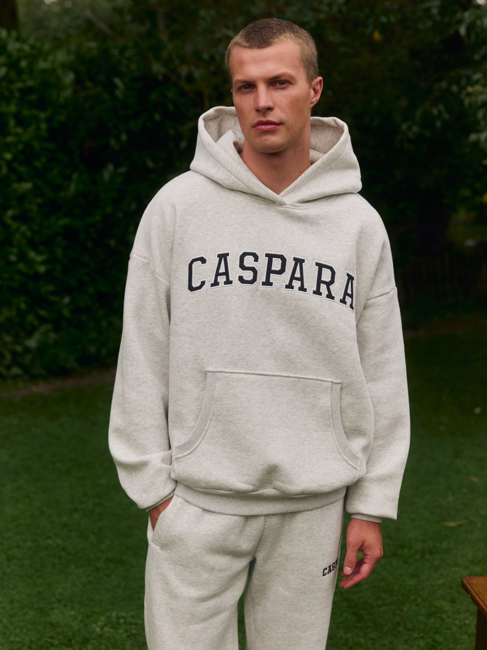 Man wearing a grey melange CASPARA hoodie and matching sweatpants outdoors.