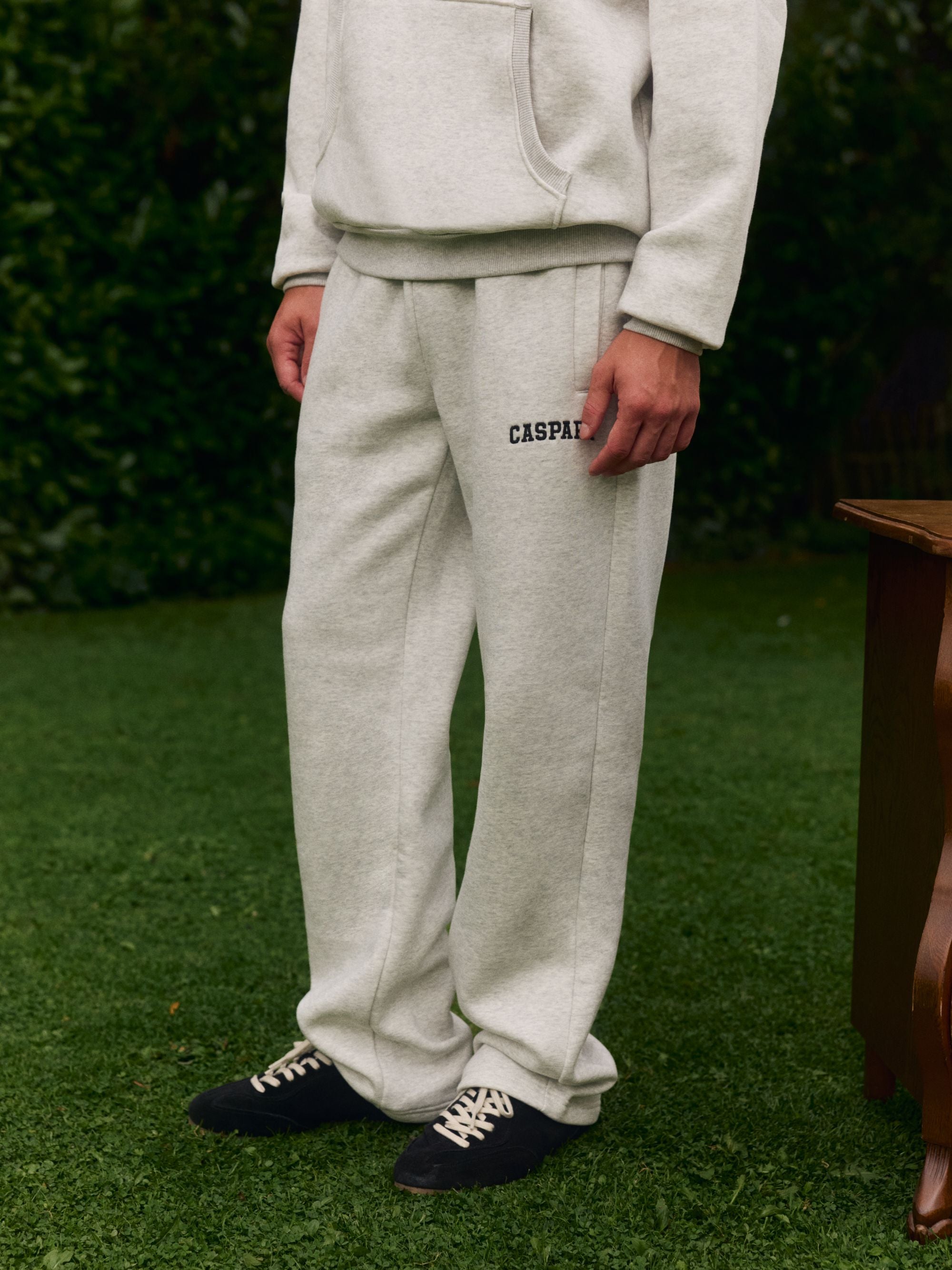 Man wearing grey melange CASPARA logo straight-leg sweatpants outdoors on grass.