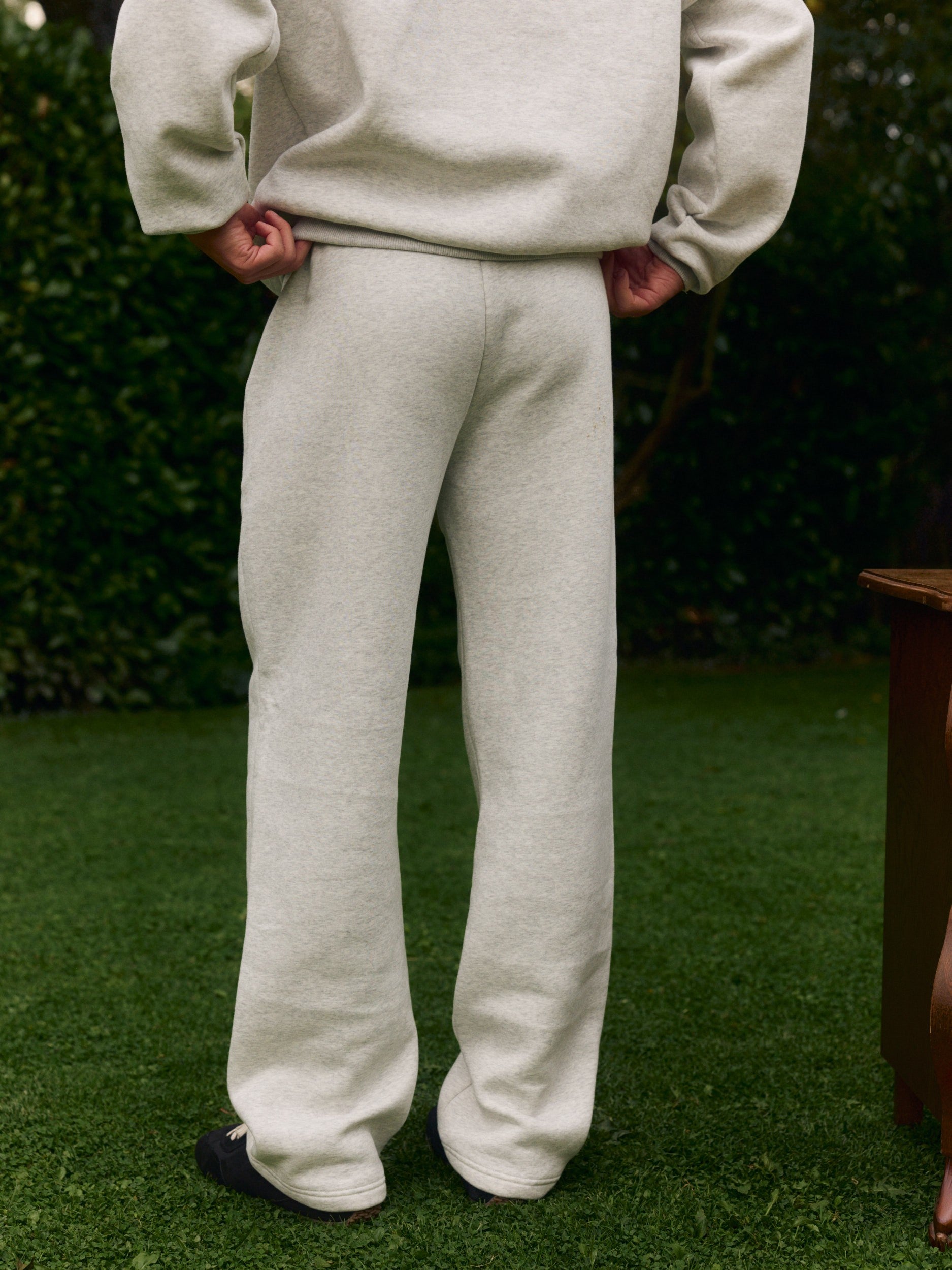 Back view of a man wearing grey melange straight-leg sweatpants standing on a green lawn.