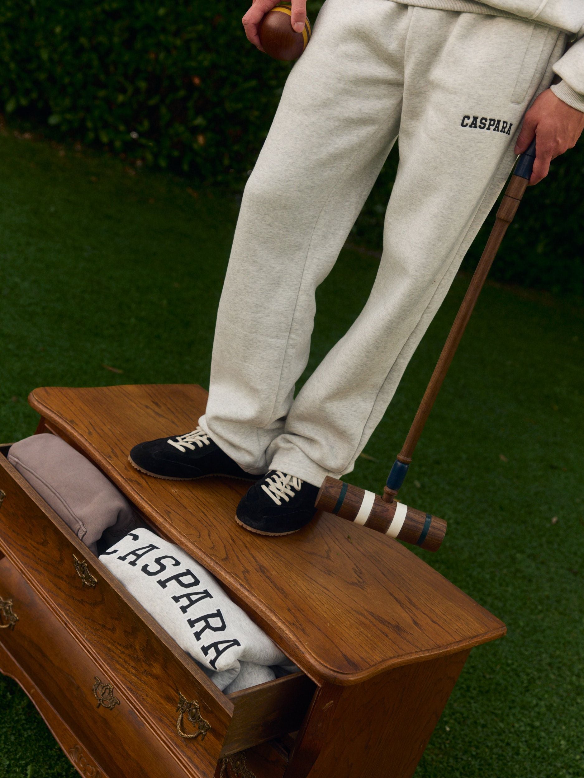 Man wearing grey melange straight-leg sweatpants standing on a wooden dresser holding a croquet mallet.