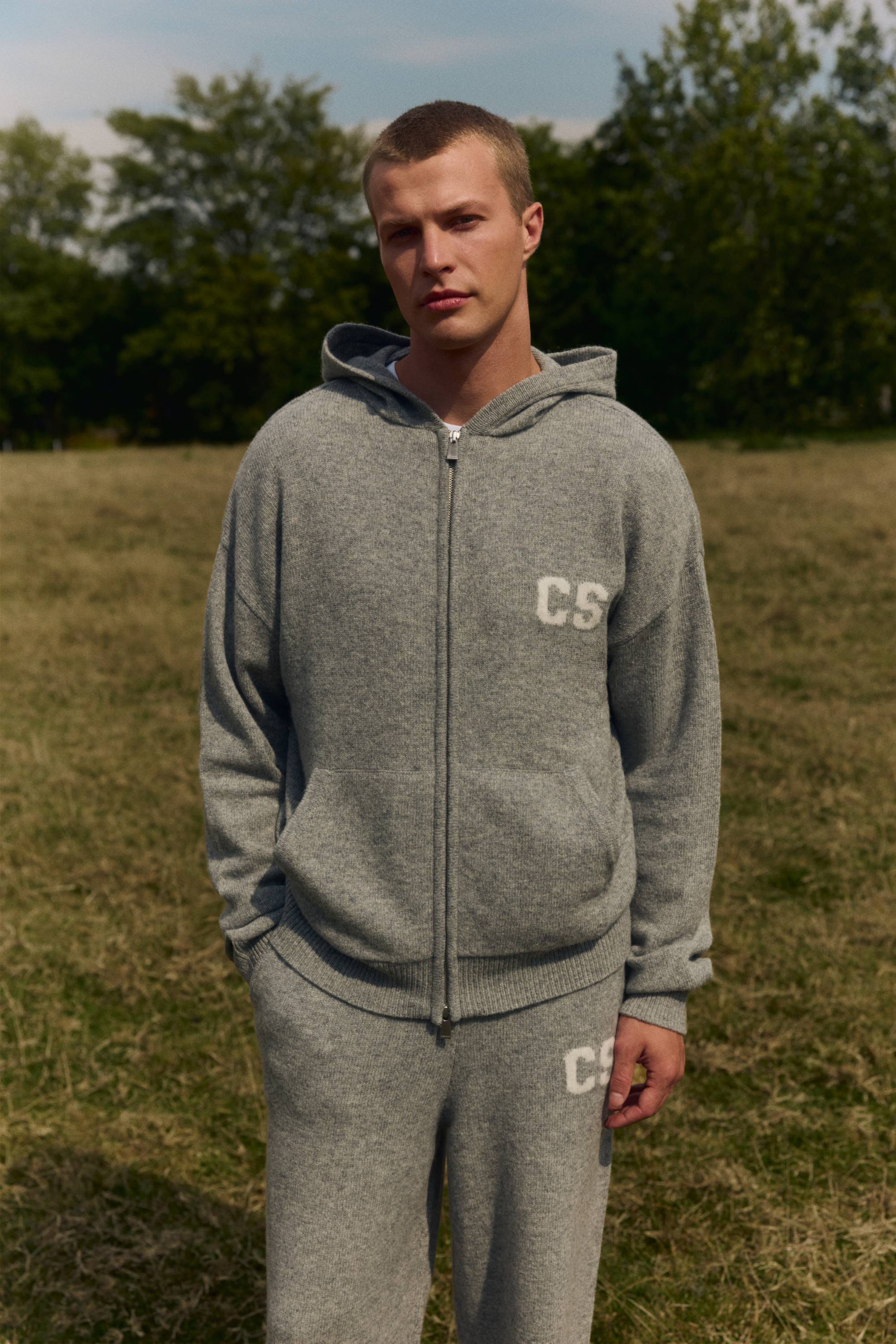 Man wearing a dark grey melange CASPARA woolknit zip jacket outdoors in a field.