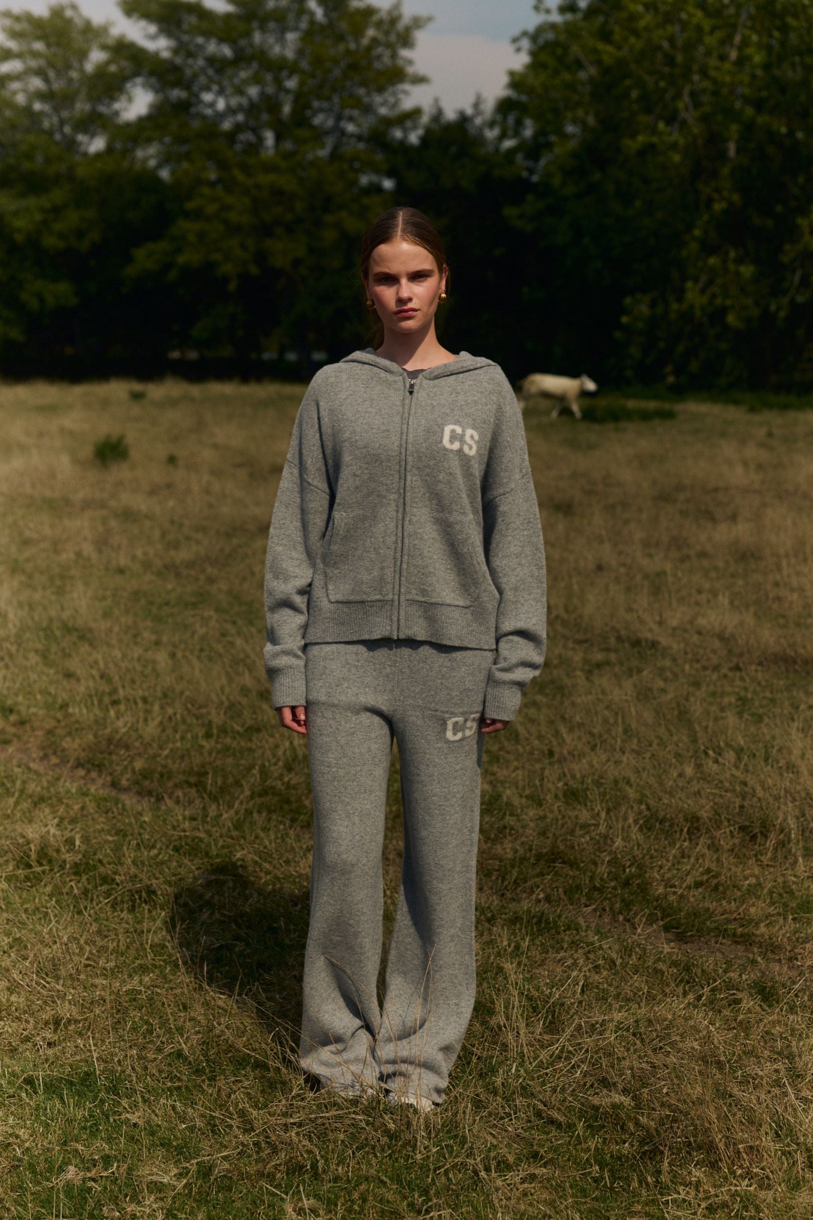 Woman wearing a grey wool knit zip-up jacket and matching knit pants in a grassy field.