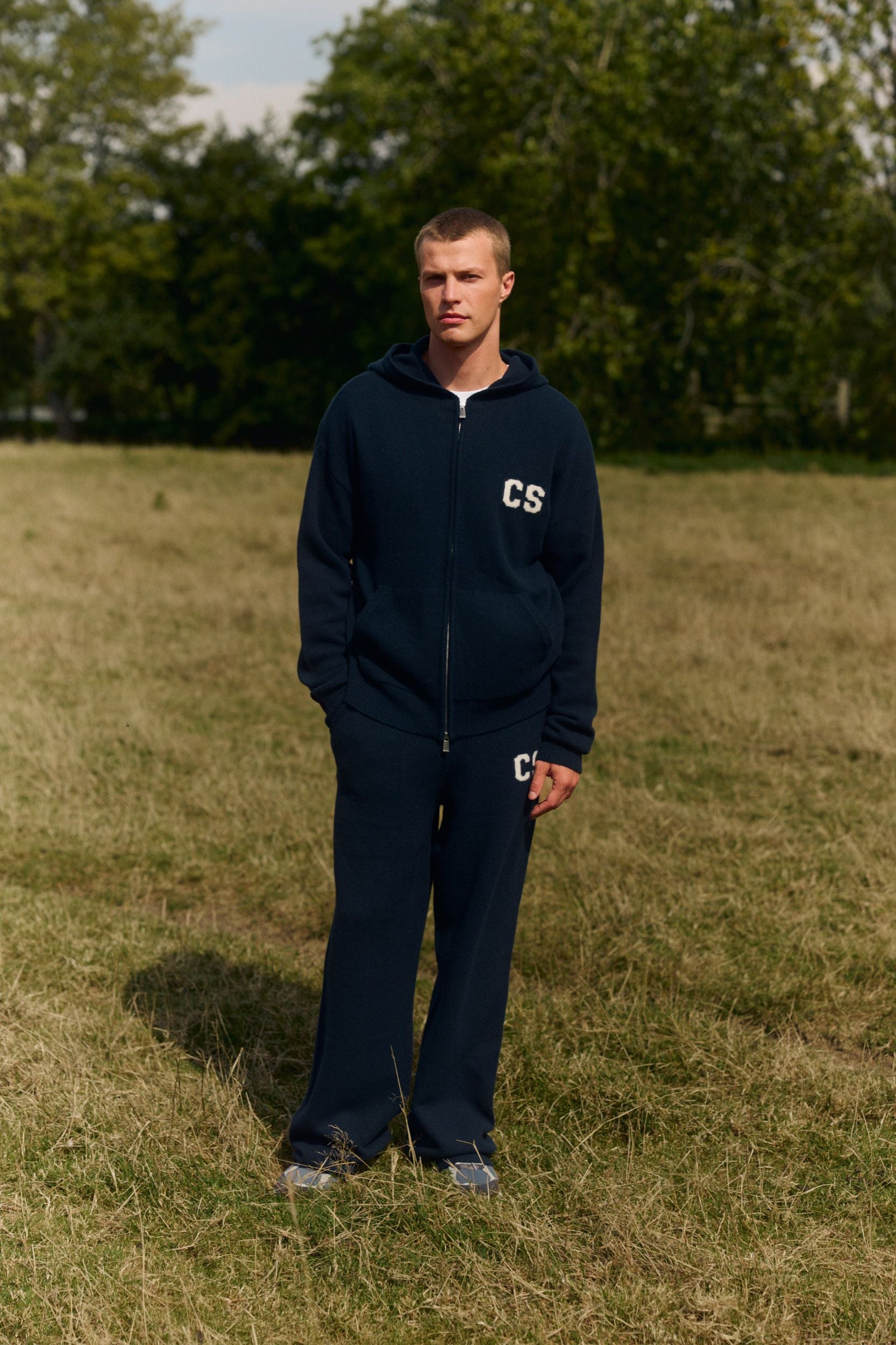 Man wearing a navy woolknit zip jacket and matching pants in a grassy field.