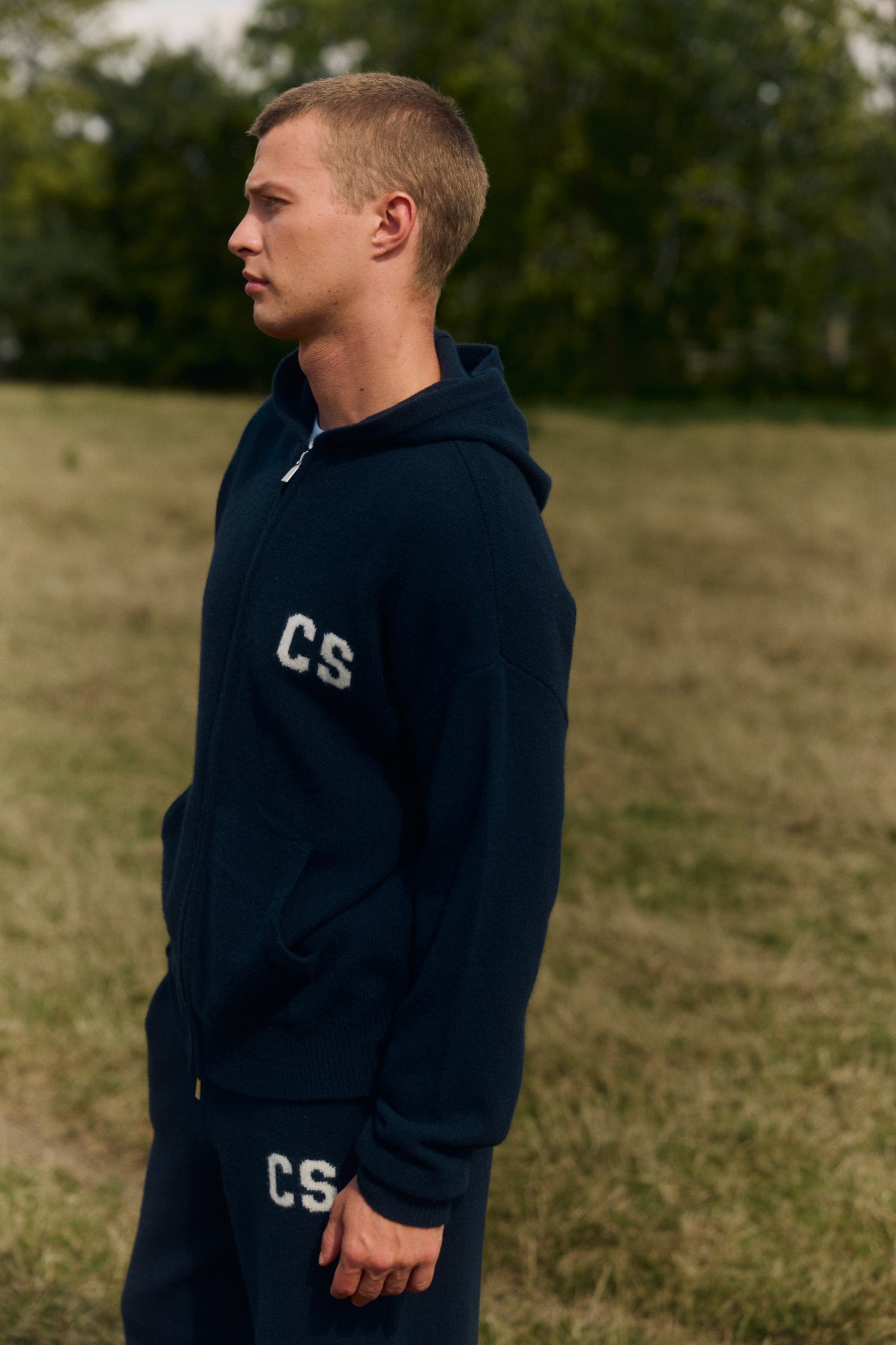 Man wearing a navy wool knit zip jacket with a CS logo in a grassy field.