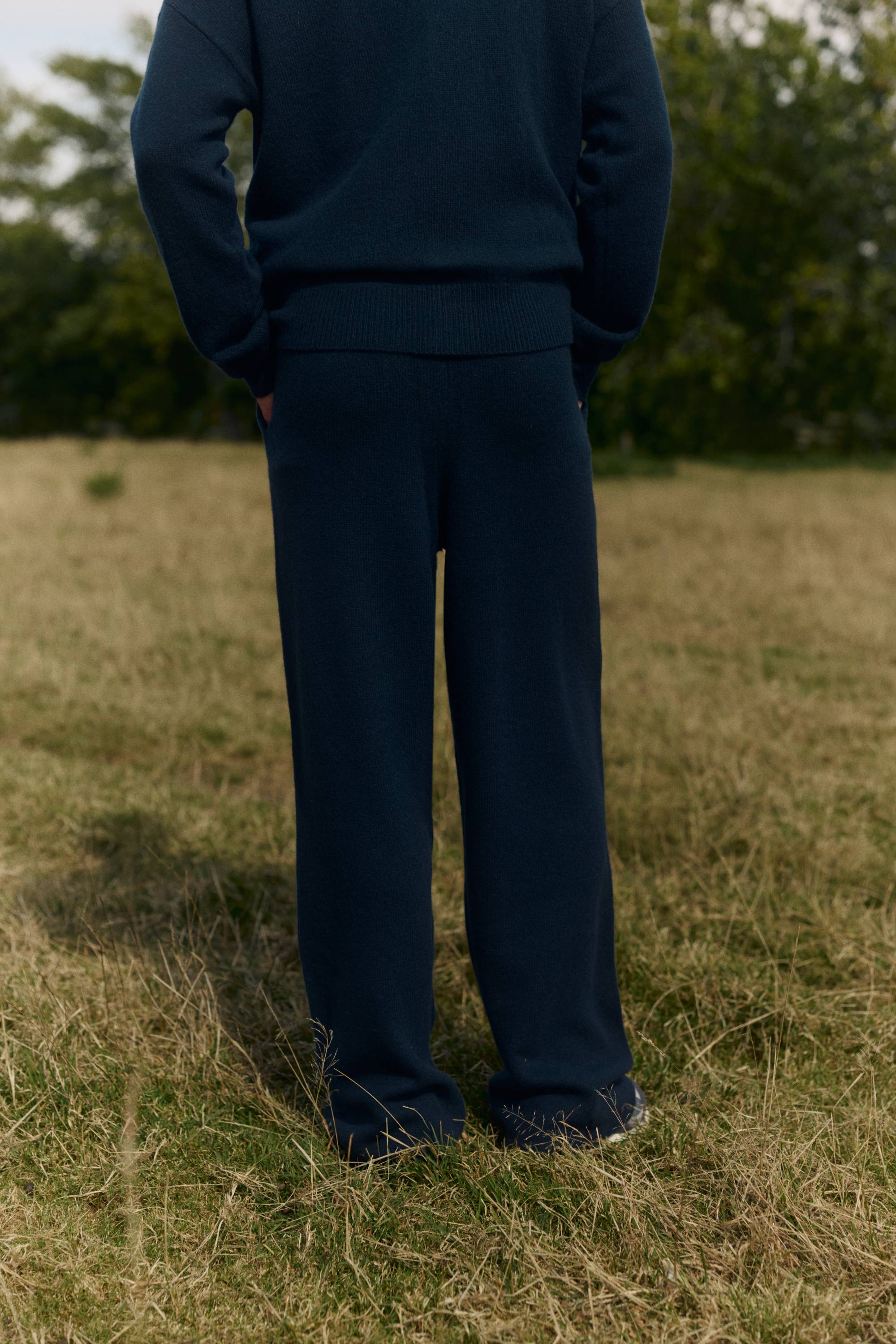 Back view of man wearing navy CASPARA woolknit straight leg pants in a field.