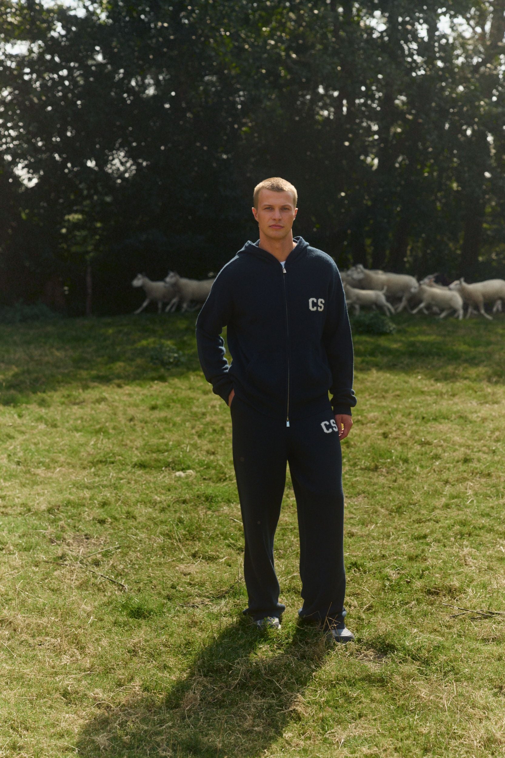 Man wearing navy woolknit straight-leg pants and matching hoodie standing in a grassy field.