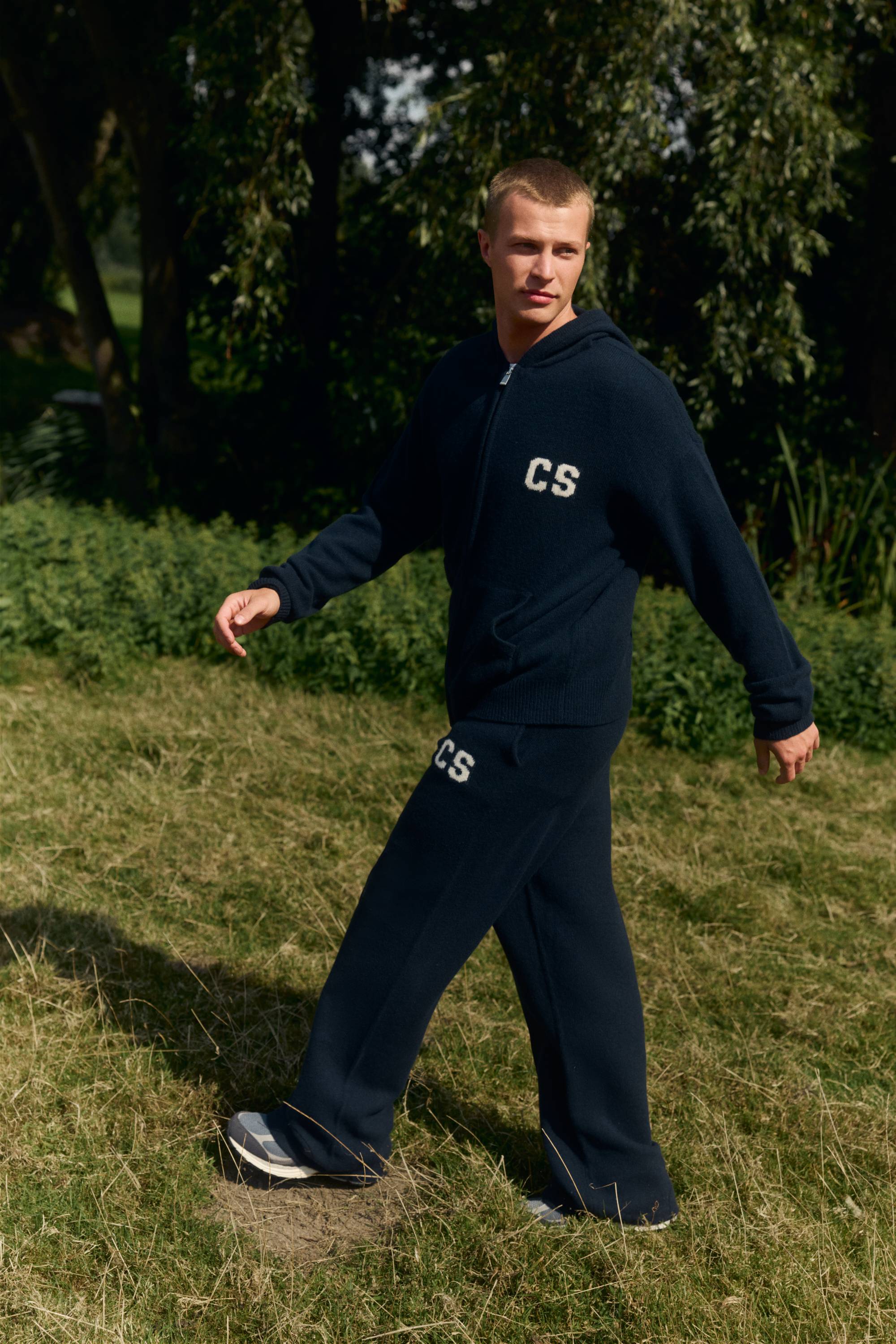 Man walking outdoors wearing navy CASPARA woolknit straight-leg pants and a matching zip hoodie.