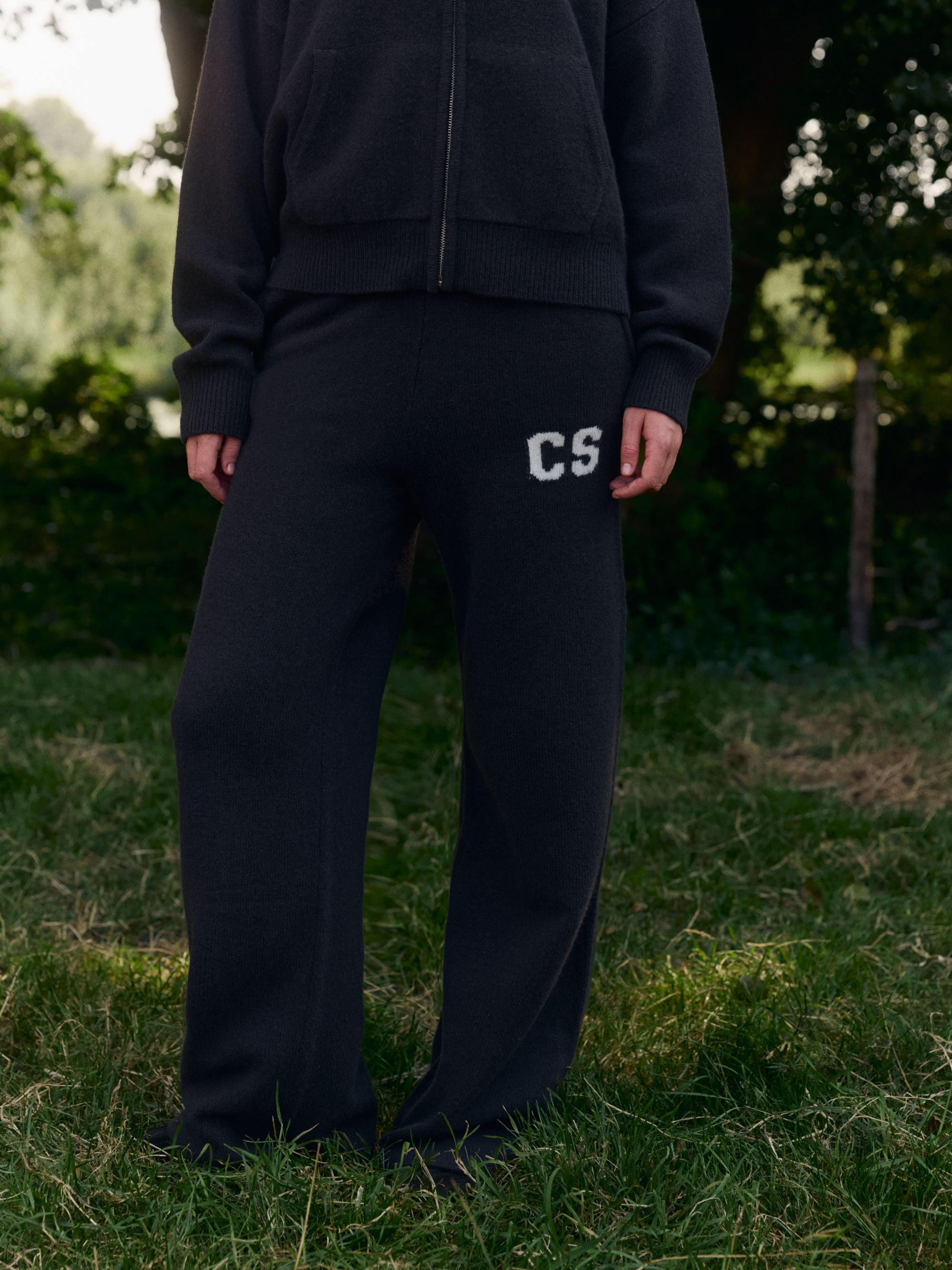 Woman wearing cocoa bean CASPARA woolknit straight-leg pants with a CS logo outdoors on grass.