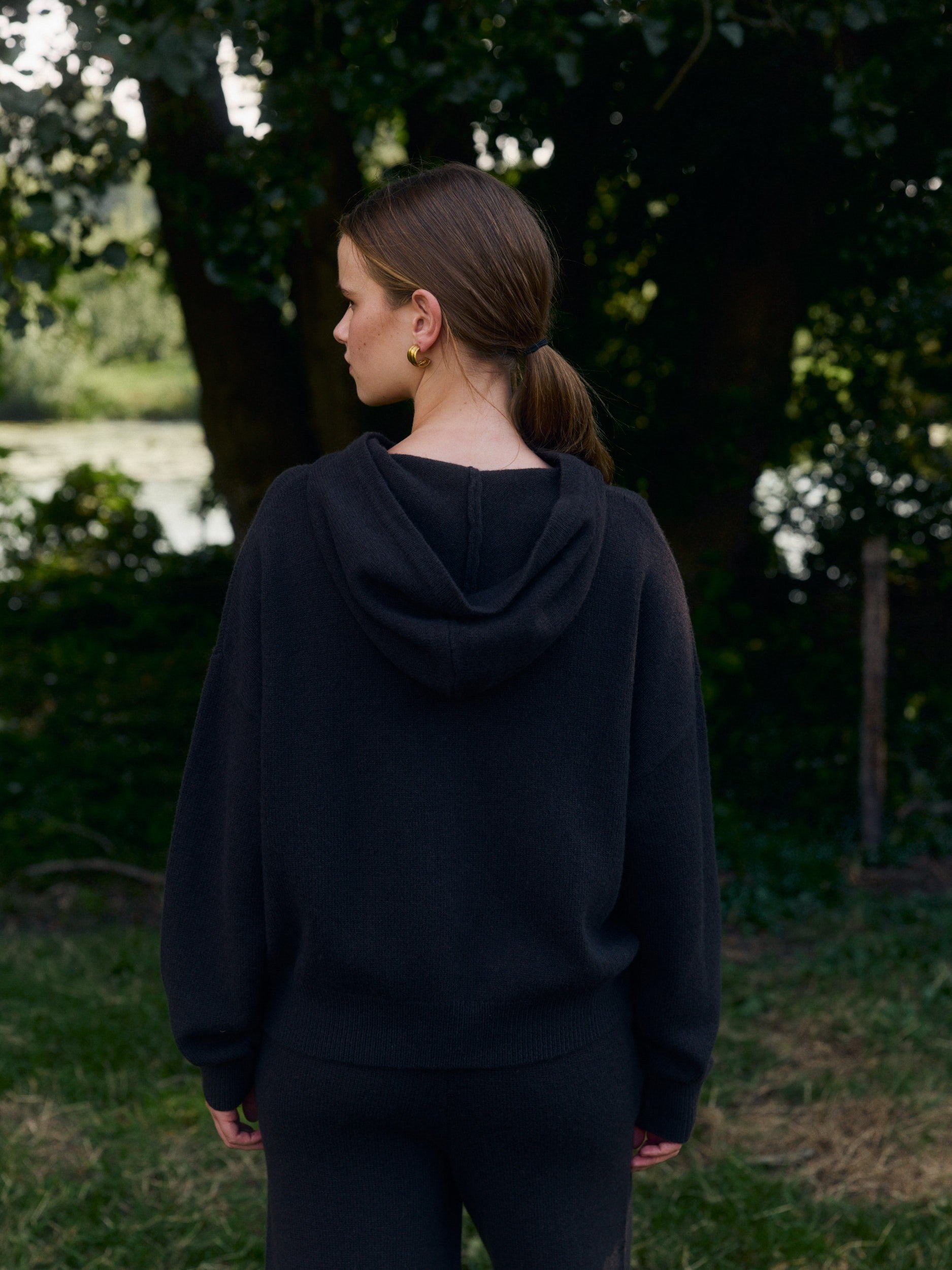 Woman seen from behind wearing a dark brown woolknit hooded jacket outdoors.