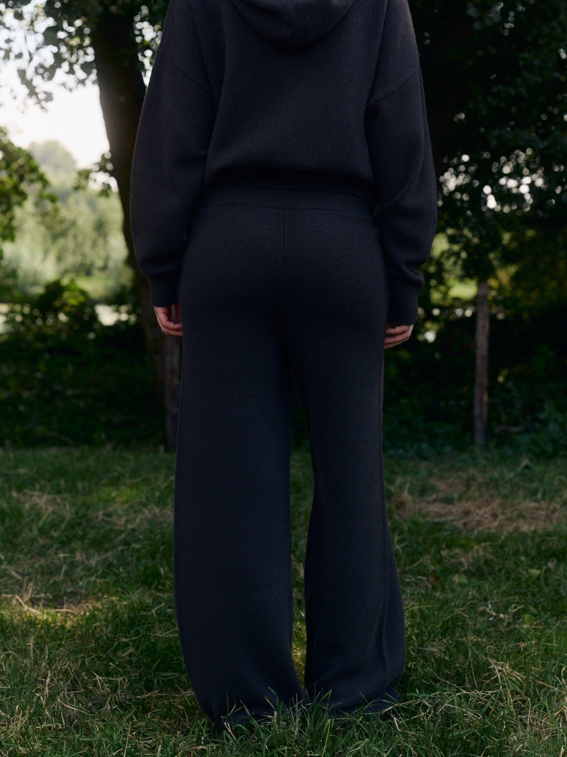 Woman wearing dark brown wool knit straight-leg pants and matching hoodie outdoors on grass.