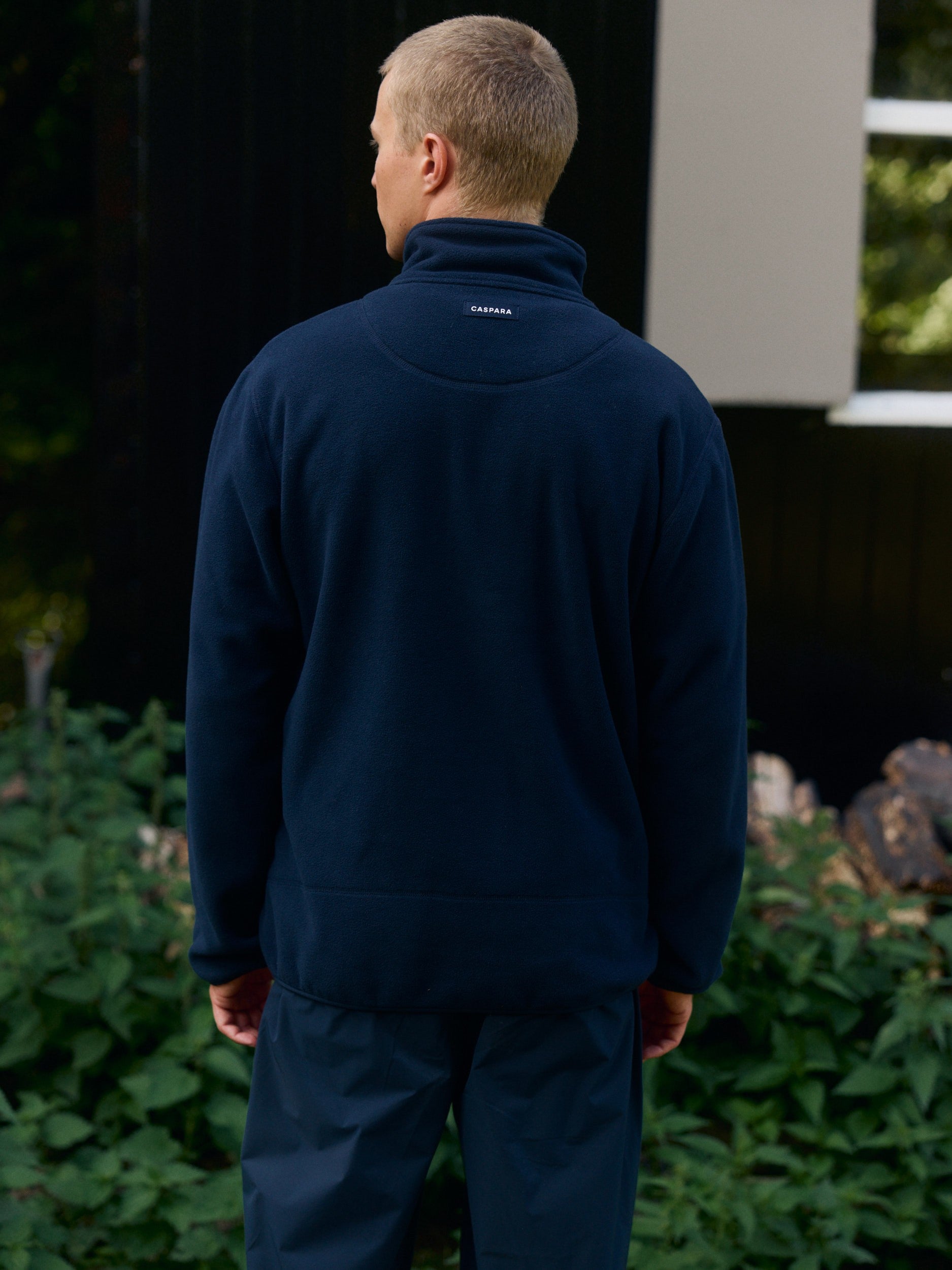Rear view of a man wearing a navy blue polar fleece pullover standing outdoors.