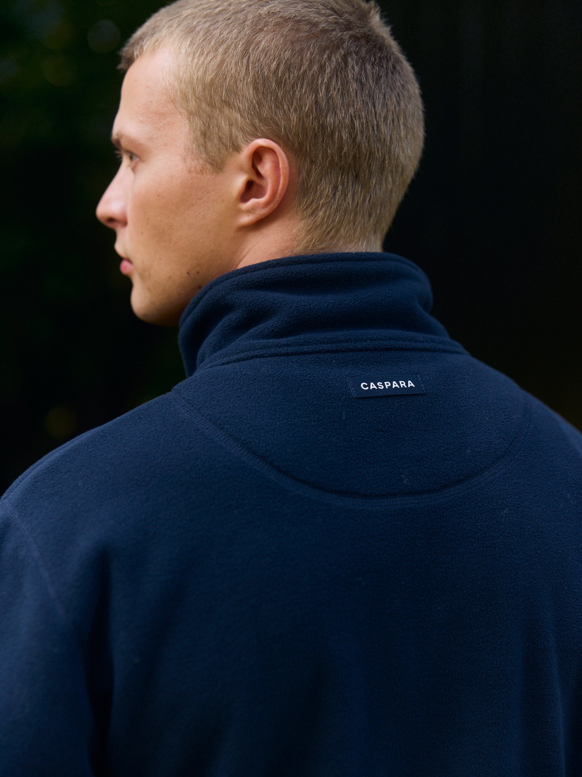 Back view of a man wearing a navy polar fleece pullover with a CASPARA logo badge.